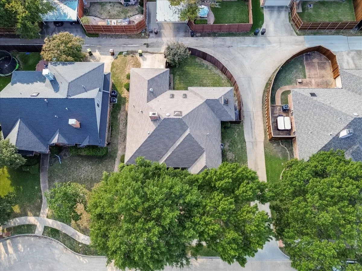Aerial perspective of a multi-gabled architectural roofline featuring chimney stacks, skylights, and composition shingles, positioned on a corner lot with a concrete driveway and mature tree canopy