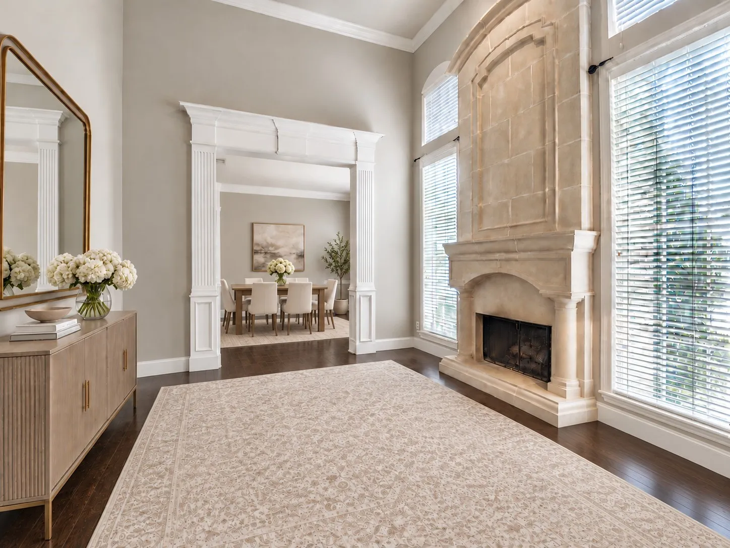 High ceilings featuring crown molding, floor-to-ceiling stone fireplace, wood-finish flooring, and classical millwork framing the doorway