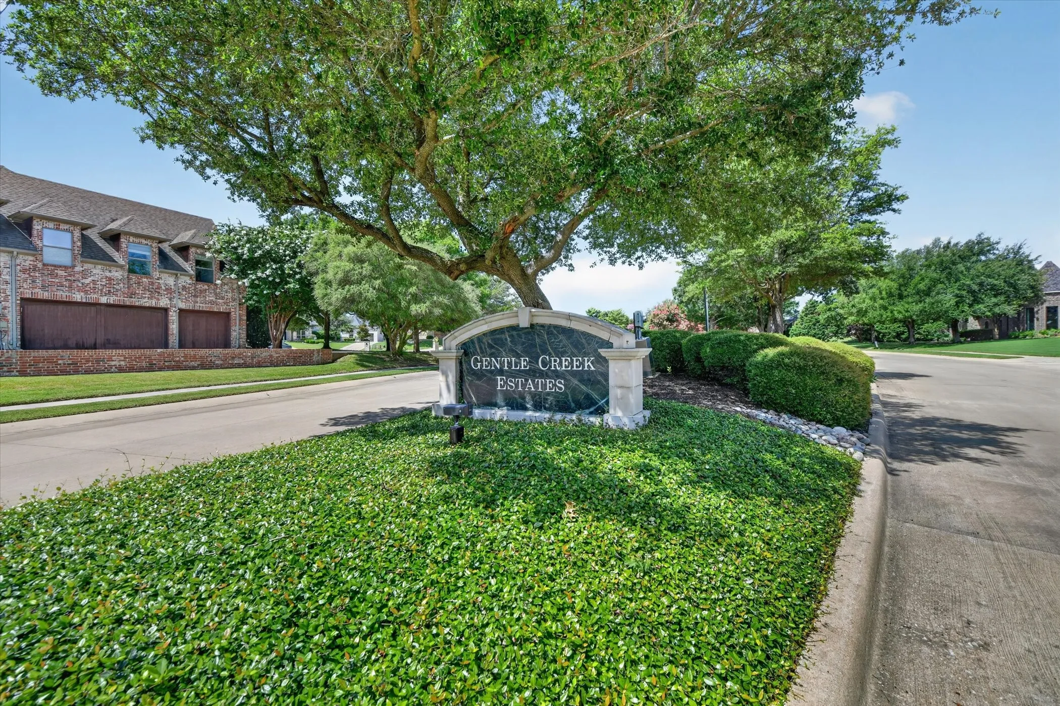 Stone community monument sign featuring integrated lighting and mature landscaping