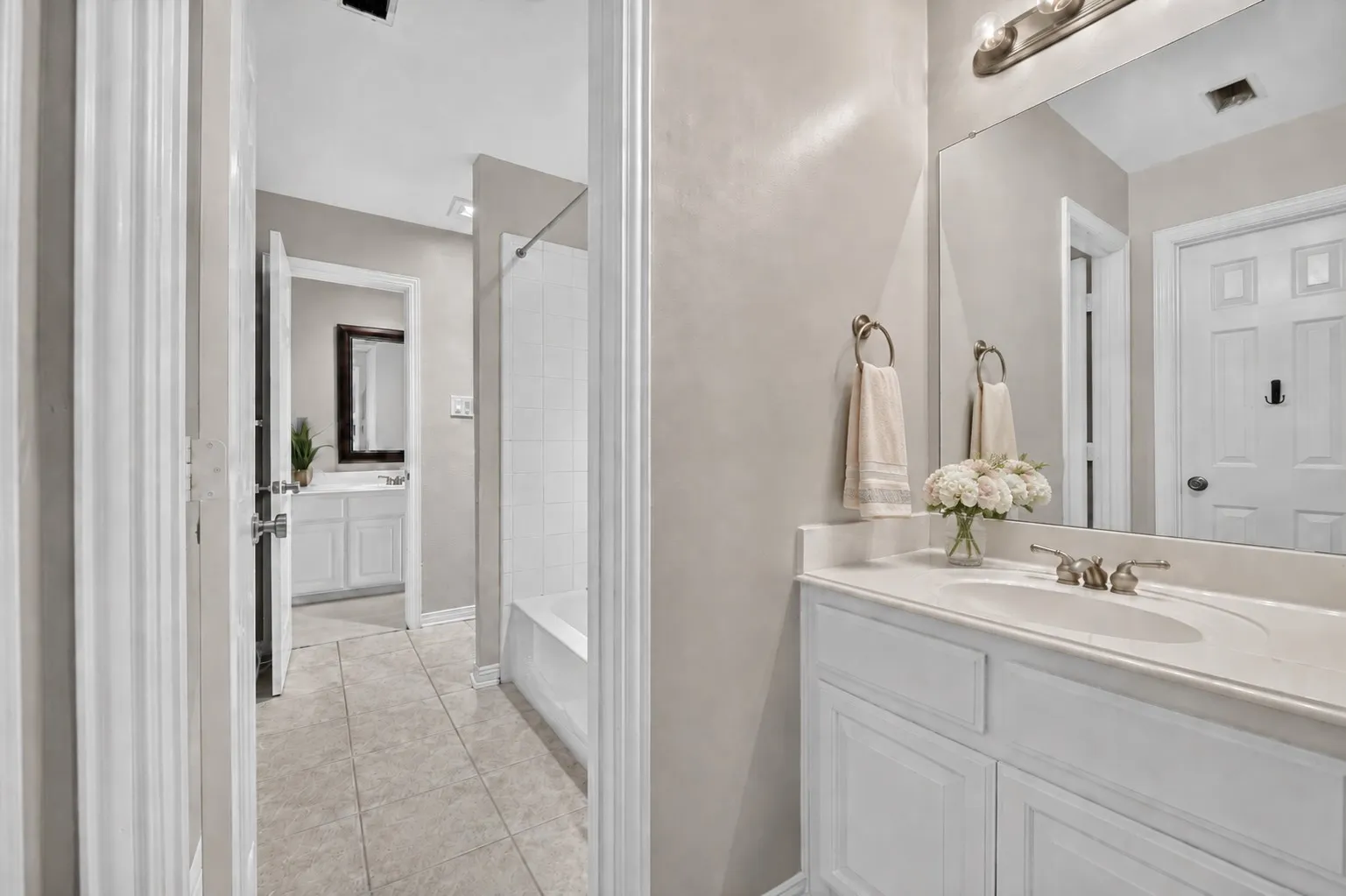 Bathroom featuring white cabinetry, an integrated sink with a polished metal faucet, a large wall-mounted mirror, and tile flooring