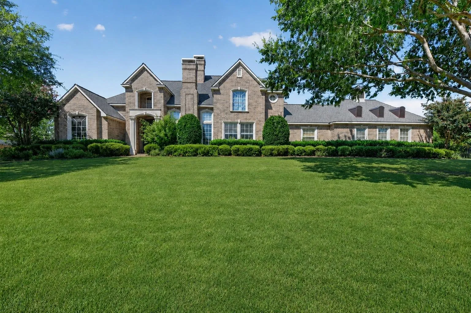 Brick exterior residence featuring a gabled roofline, central chimney, multi-pane windows, and extensive landscaping