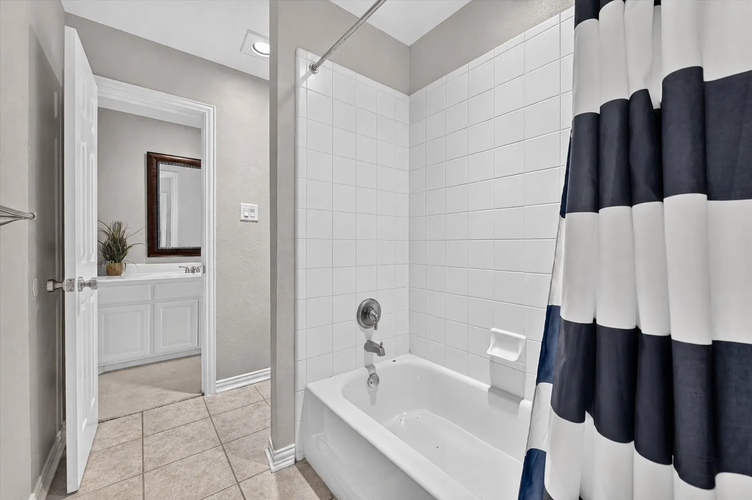 Full-height white tile shower surround, integrated tub, light-toned ceramic tile flooring, built-in white vanity cabinetry, and a wall-mounted rectangular mirror
