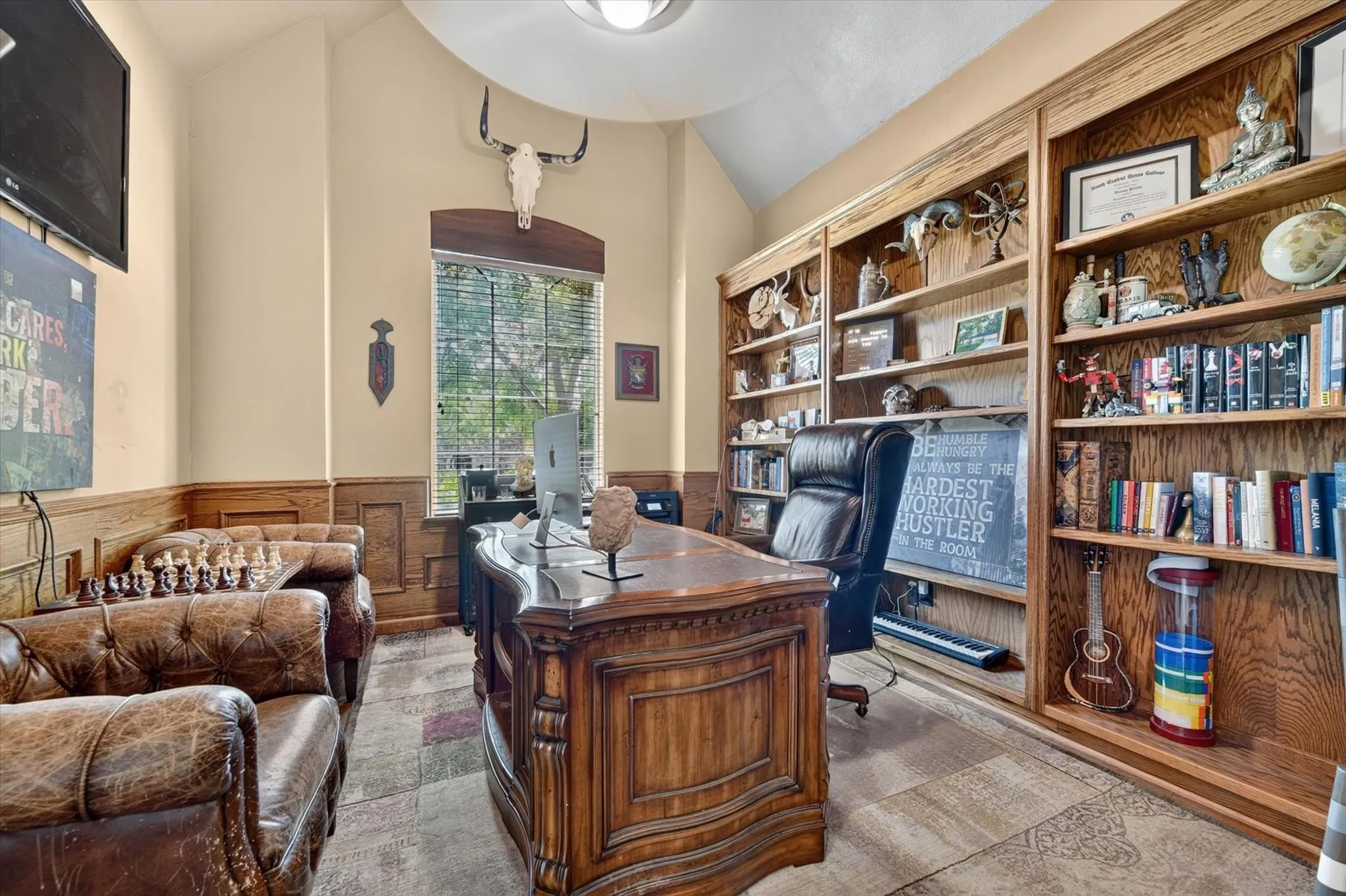 Vaulted ceiling with a centered light fixture, extensive floor-to-ceiling built-in wood shelving, wood wainscoting, and a central window with an arched wood header