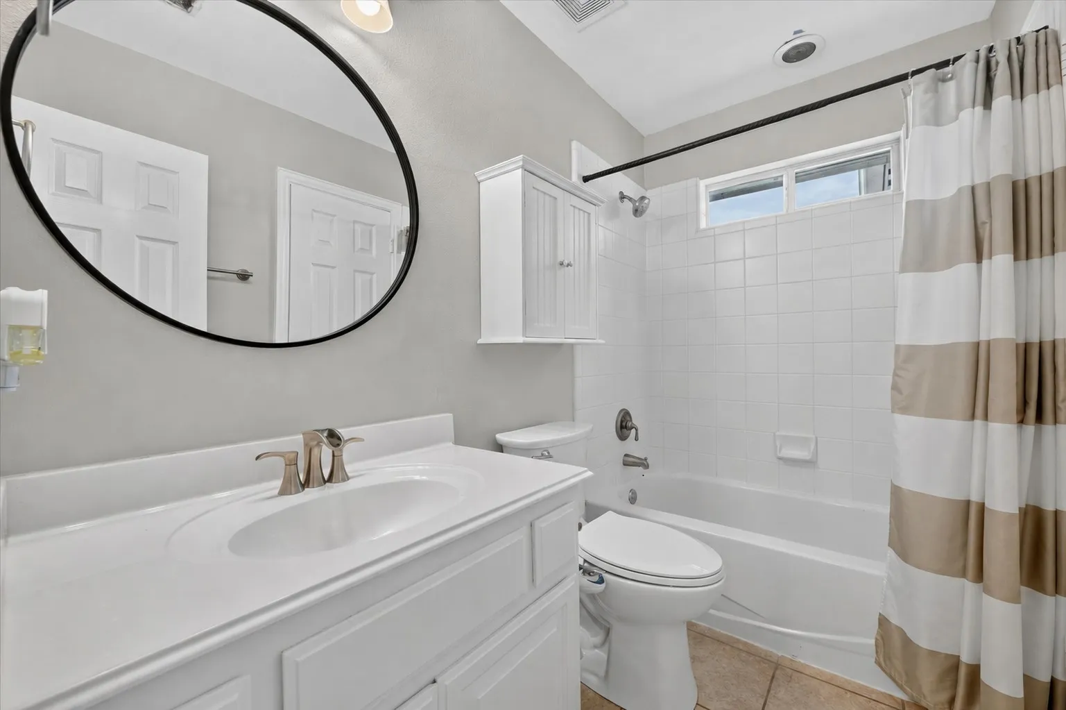 Bathroom featuring a vanity with an integrated basin, a large oval mirror, a wall-mounted medicine cabinet, and a tiled shower-tub combination