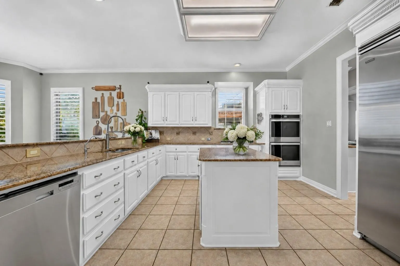 Kitchen featuring white cabinetry, stone-surface countertops, tile flooring, a center island, and stainless steel double wall ovens