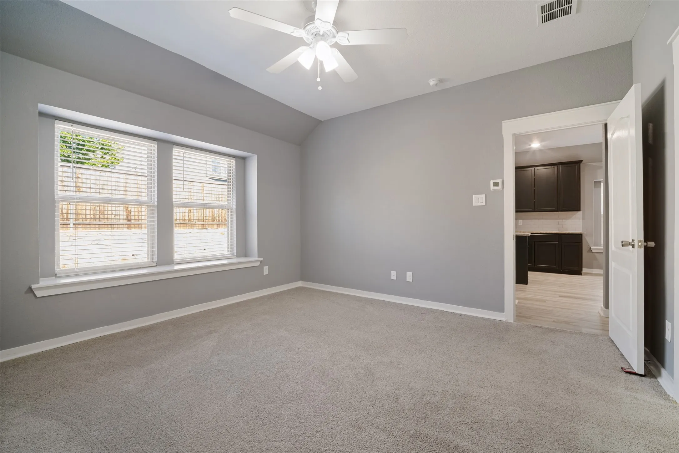 Neutral-toned room featuring a vaulted ceiling, bay window with sill, carpeted flooring, and a ceiling-mounted fan with light fixture