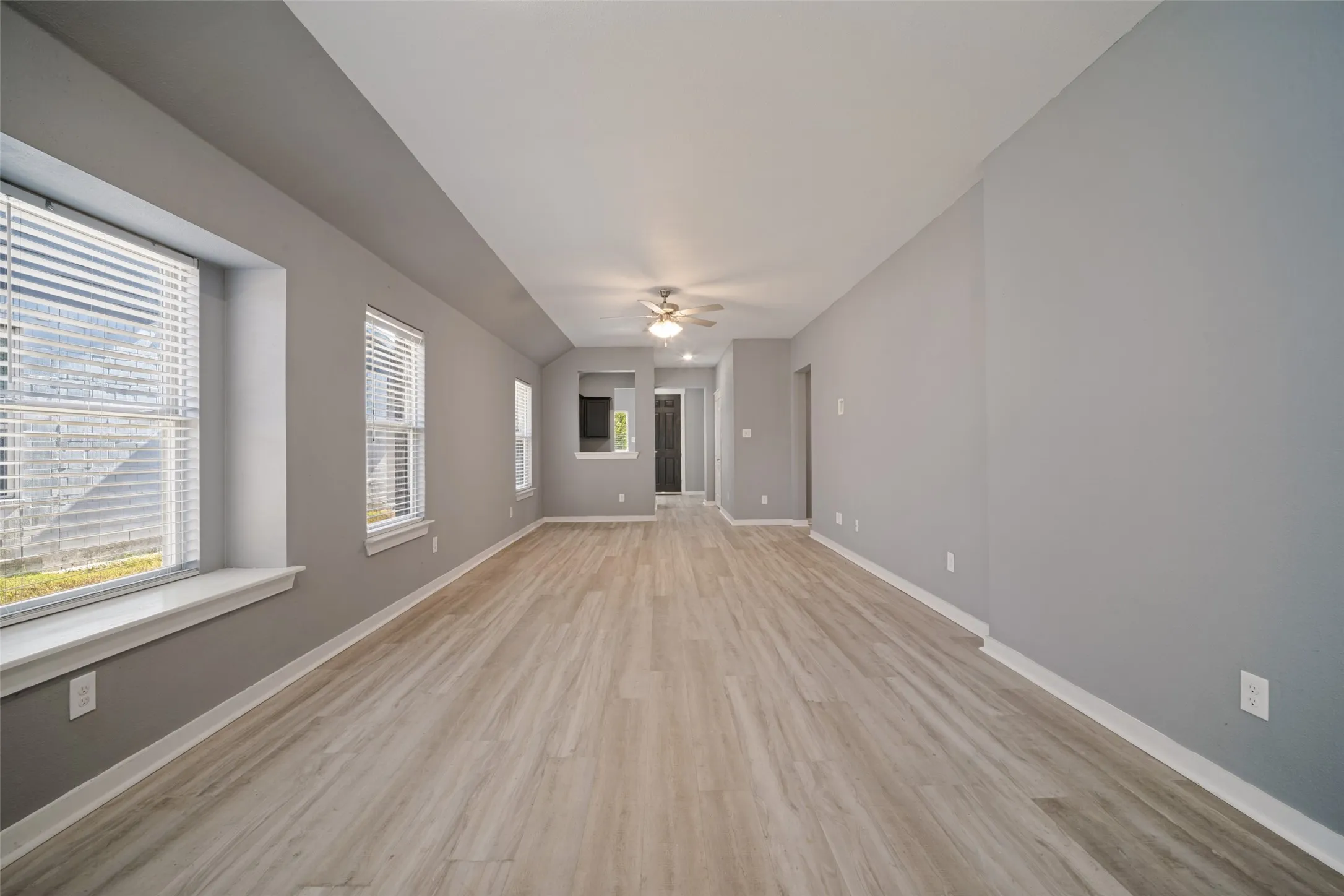 Spacious interior featuring wood-finish flooring, recessed windows with built-in sills, and a centrally mounted ceiling fan with integrated lighting