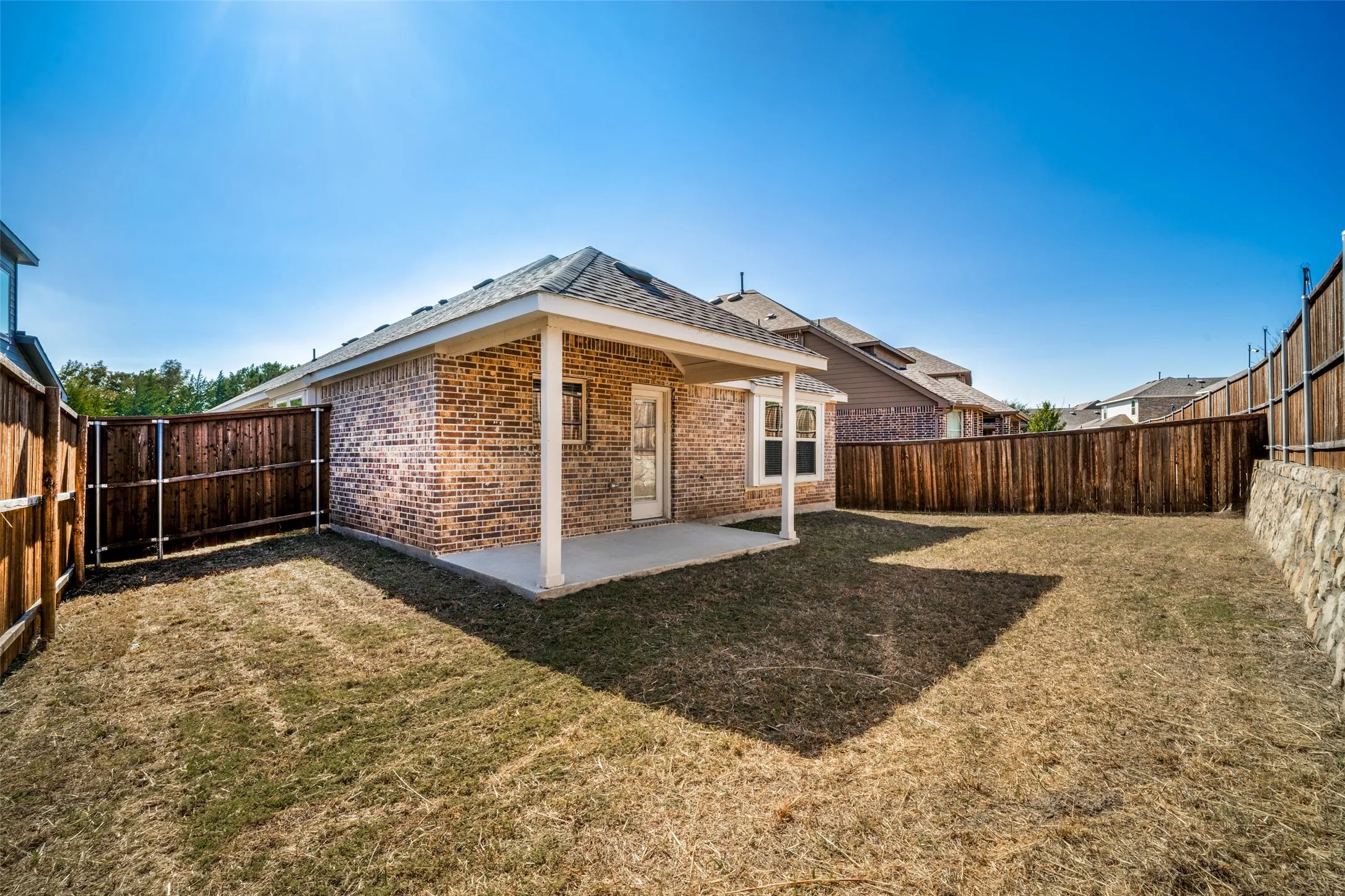 Brick exterior featuring a covered patio, concrete flooring, and surrounding wood privacy fencing with stone retaining wall elements