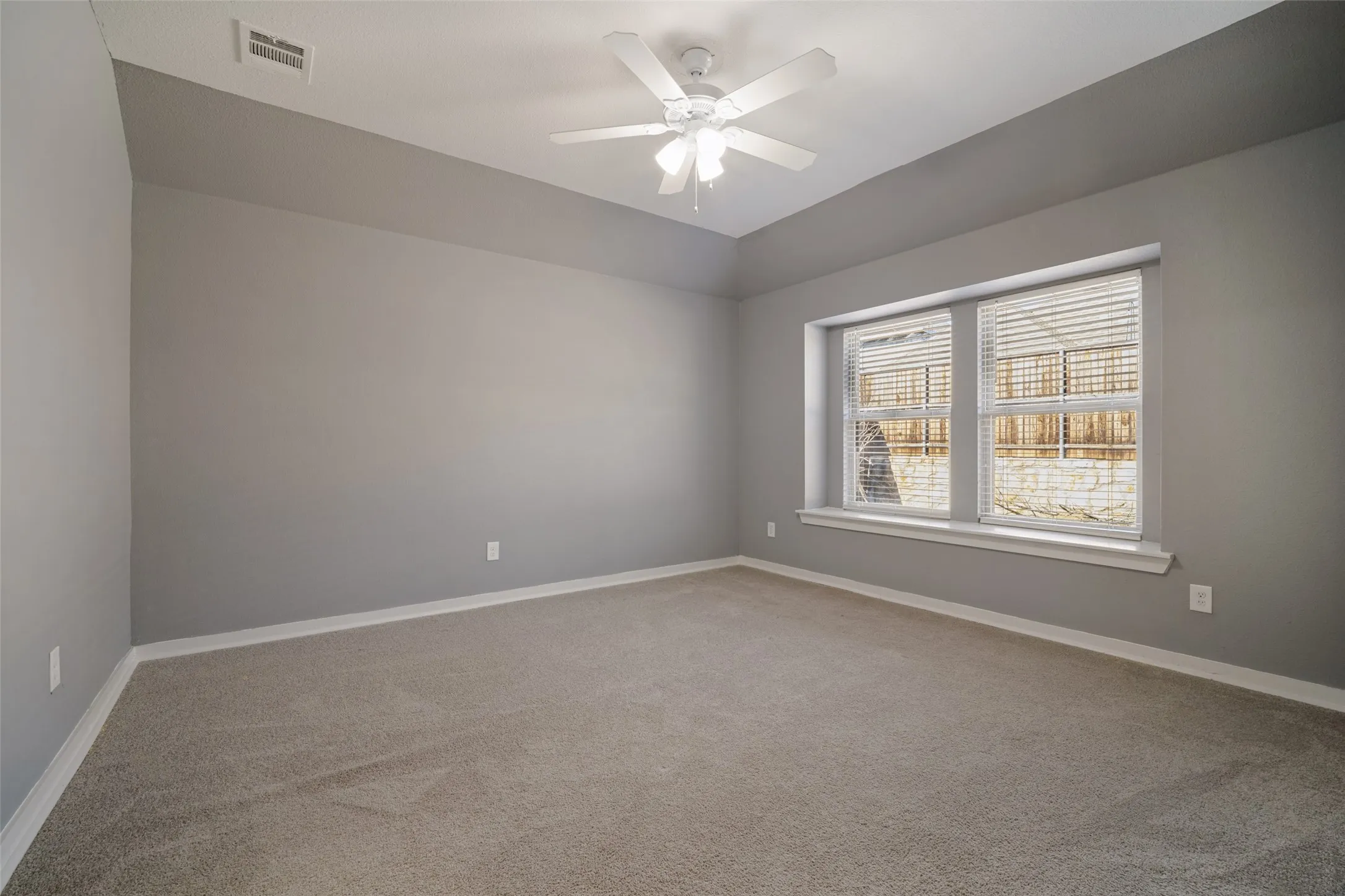 Room featuring neutral carpeting, tray ceiling, multi-blade ceiling fan with integrated lighting, and a dual-pane bay window