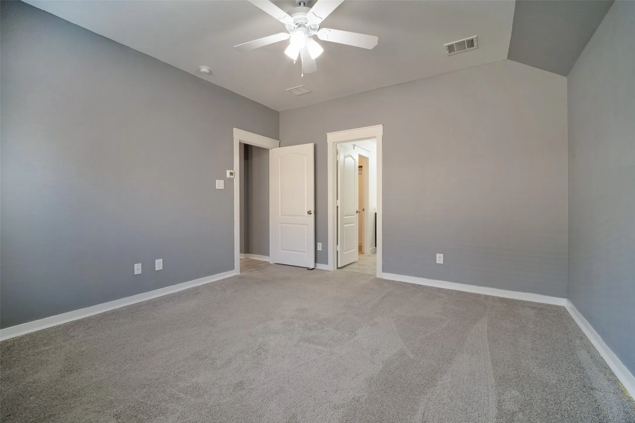 Vaulted ceiling featuring a central ceiling fan with integrated lighting, neutral wall paint, and wall-to-wall carpeting