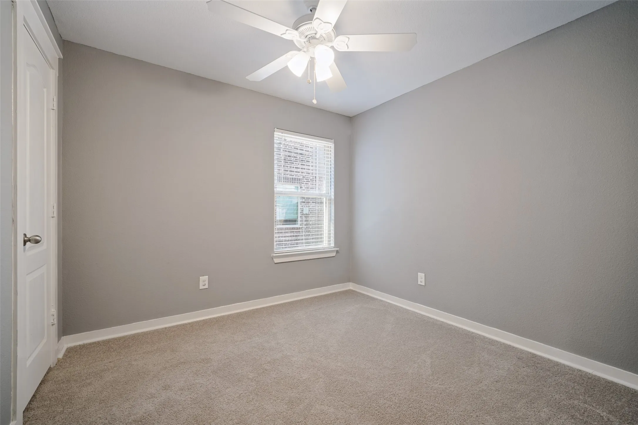 Neutral-toned interior featuring wall-to-wall carpeting, a white ceiling fan with integrated lighting, a single window with horizontal blinds, and a paneled interior door