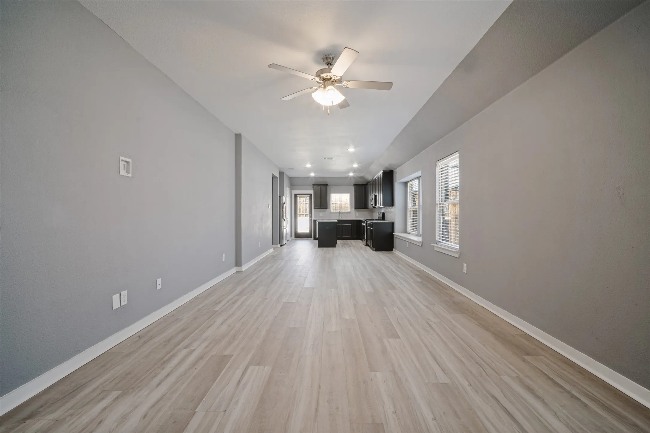 Open-concept interior featuring wood-finish flooring, vaulted ceilings with a centered ceiling fan, and recessed lighting