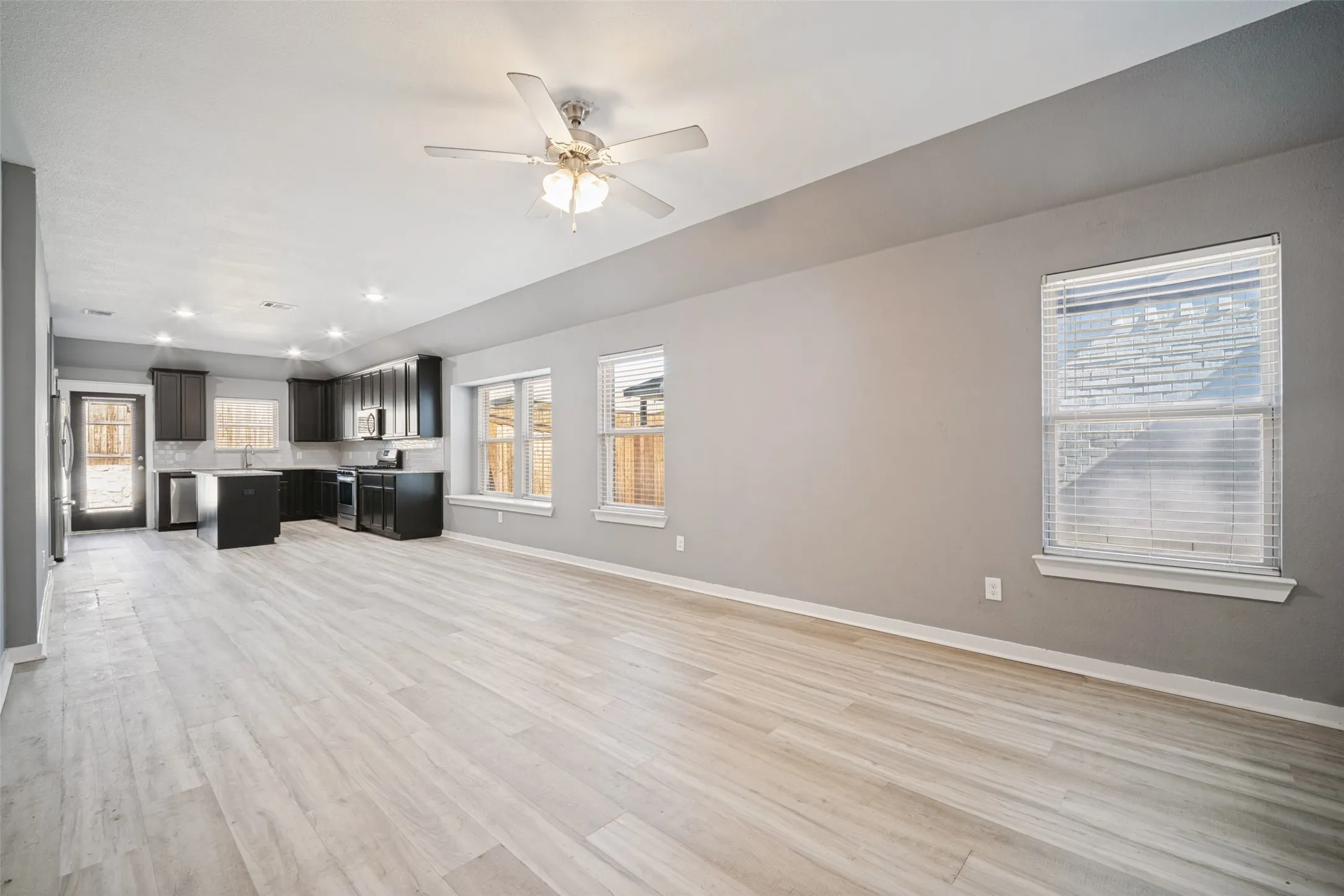 Open-concept interior featuring wood-finish flooring, dark cabinetry, a central kitchen island, recessed lighting, and a ceiling fan