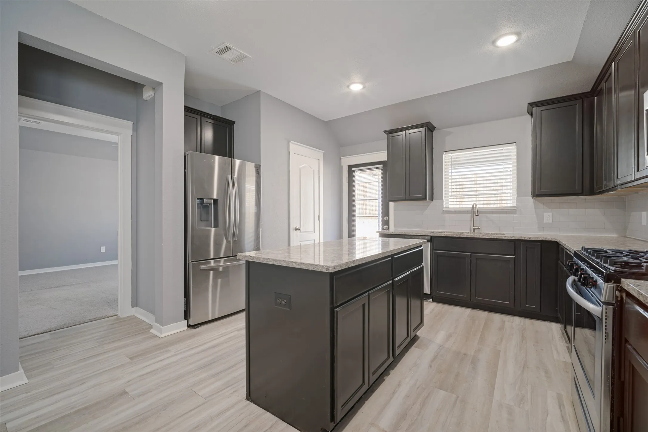 Kitchen featuring dark cabinetry, stone-surface countertops, central island, stainless steel appliances, and wood-finish flooring