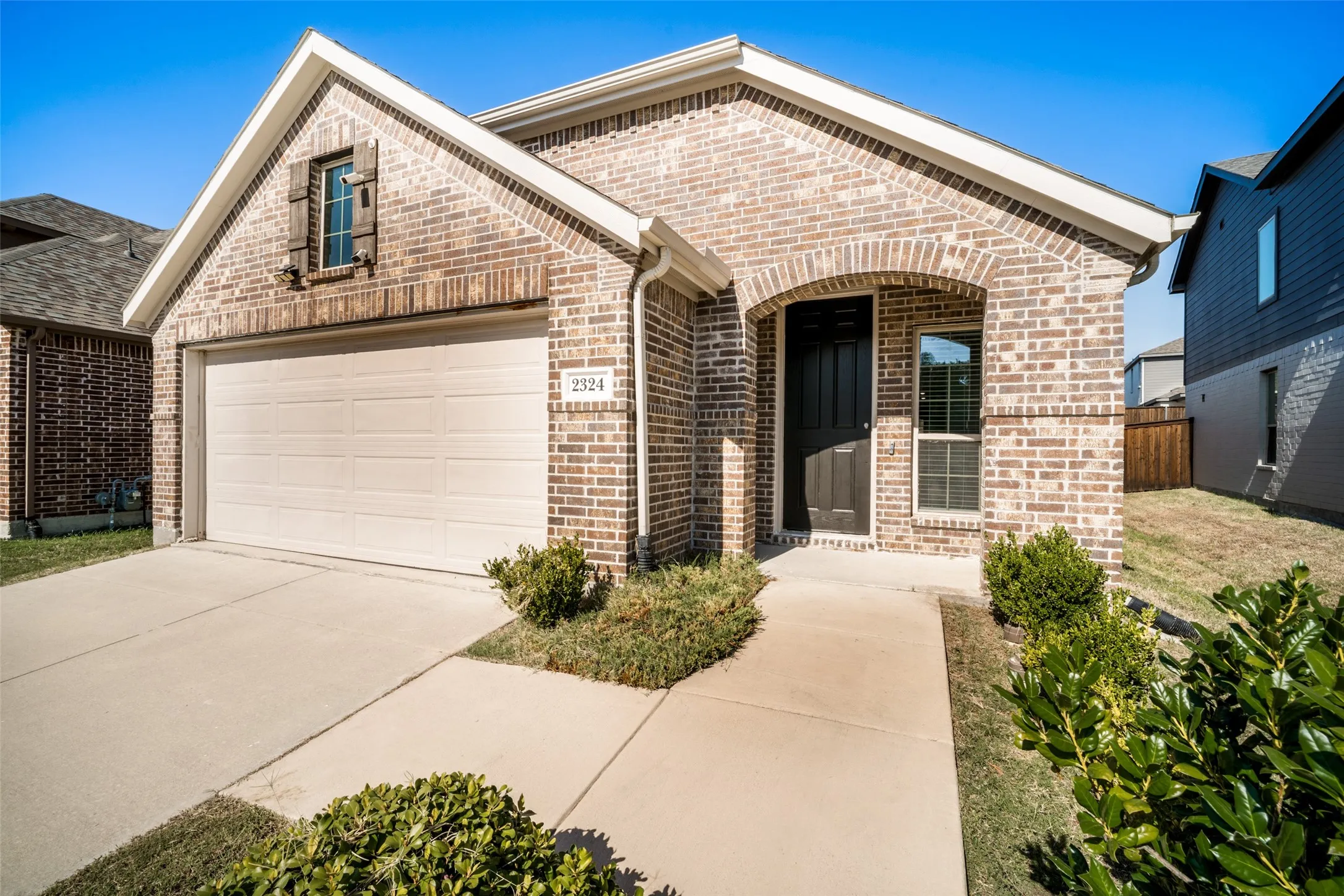 Brick exterior featuring a gabled roofline, recessed arched entryway, two-car garage, and low-maintenance landscaping