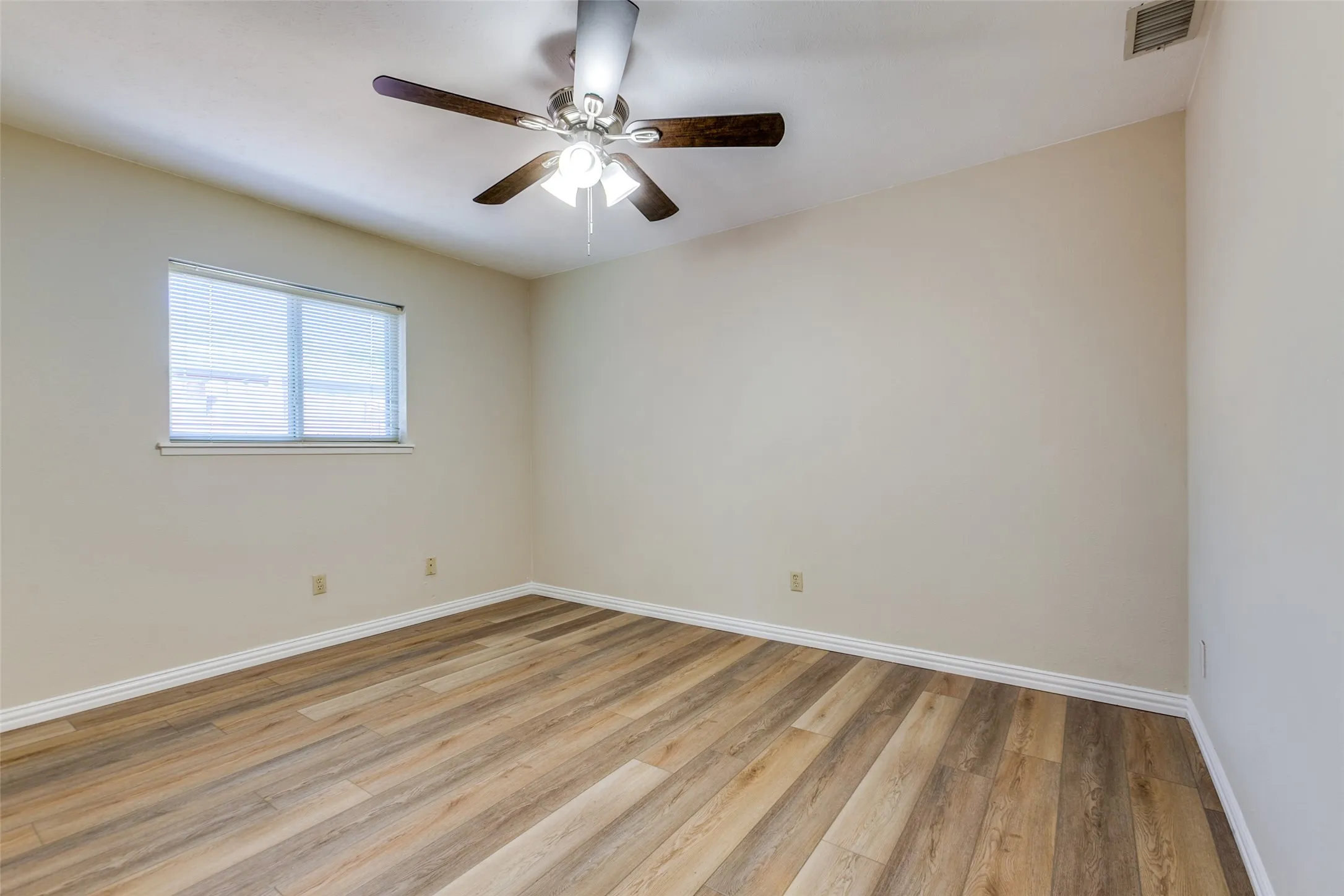Room featuring wood-finish flooring, neutral wall paint, and a ceiling-mounted fan with integrated lighting