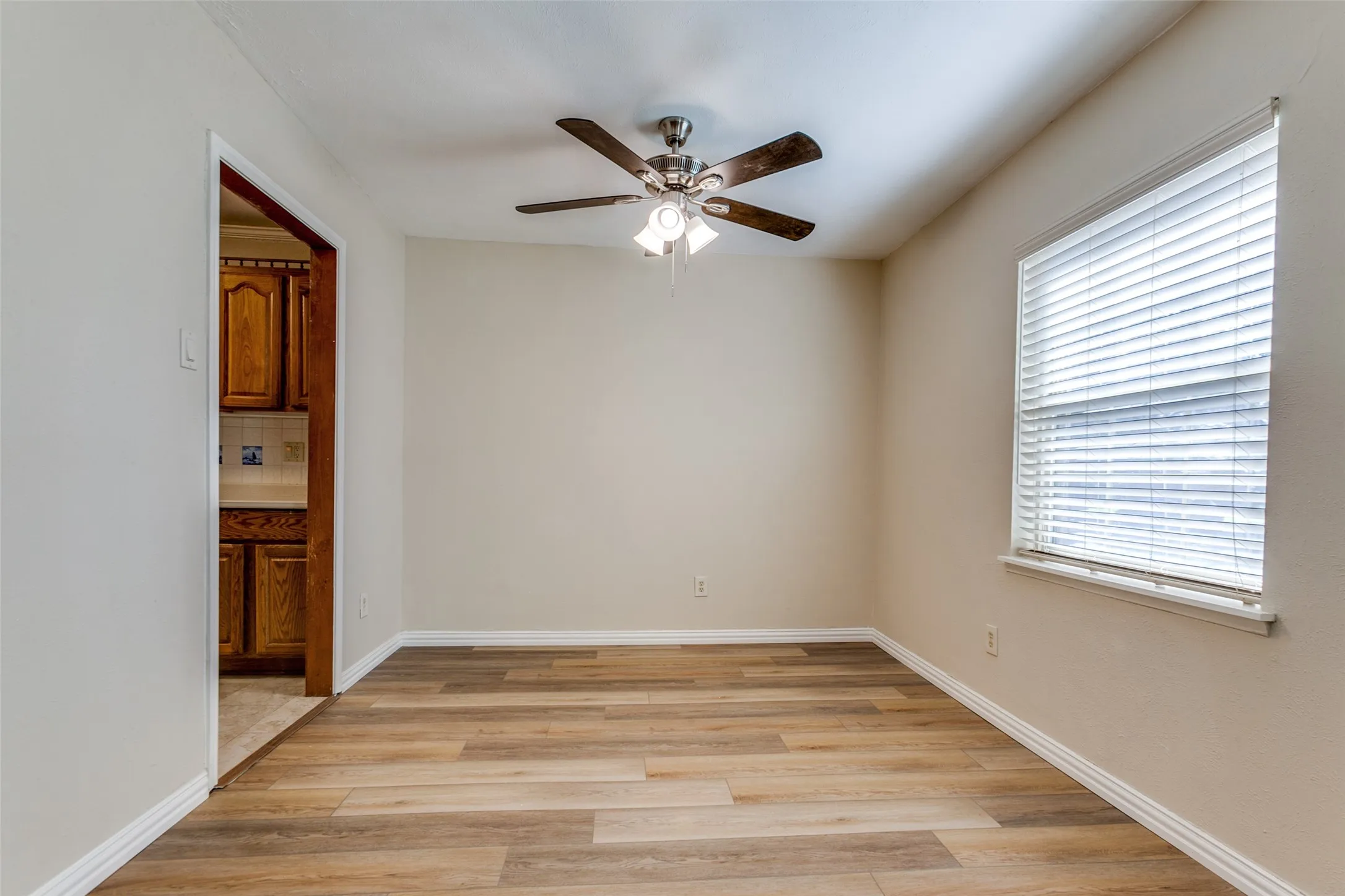 Room featuring wood-finish flooring, a ceiling fan with integrated lighting, and a window with horizontal blinds