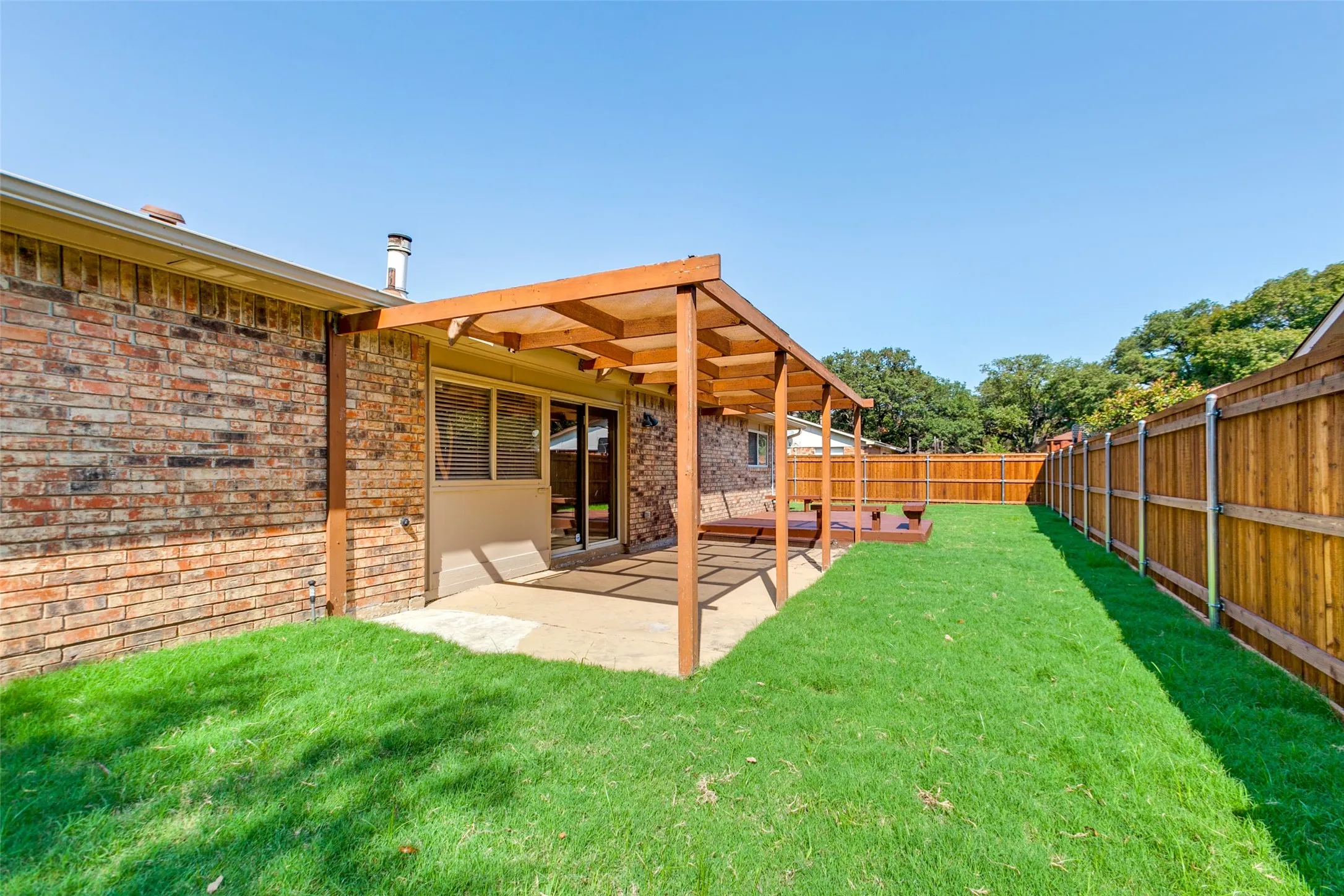 Brick exterior, wood-framed pergola, concrete patio, and perimeter wood fencing