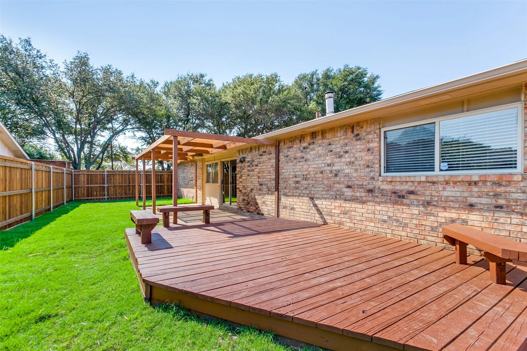 Backyard featuring a multi-level wood deck, built-in wooden bench seating, a wood-frame pergola, brick exterior siding, and a wooden privacy fence