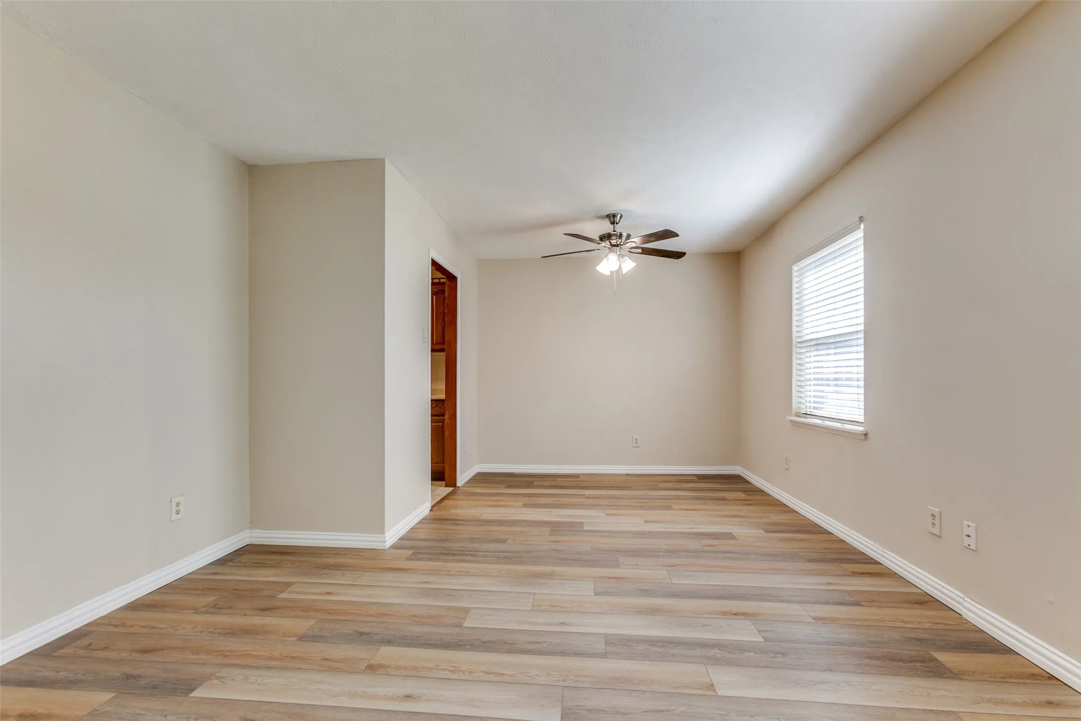 Neutral interior featuring wood-finish flooring, a ceiling fan with integrated lighting, and a window with blinds