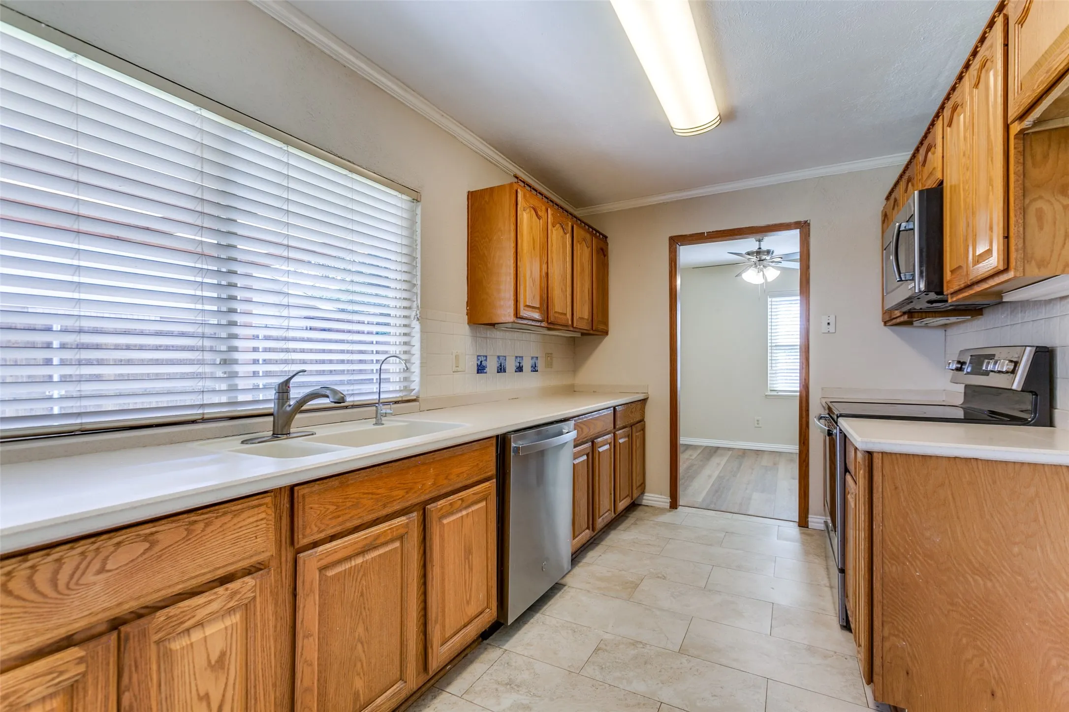 Kitchen featuring natural wood cabinetry, white countertops, a dual-basin sink with a gooseneck faucet, stainless steel dishwasher, and tiled flooring