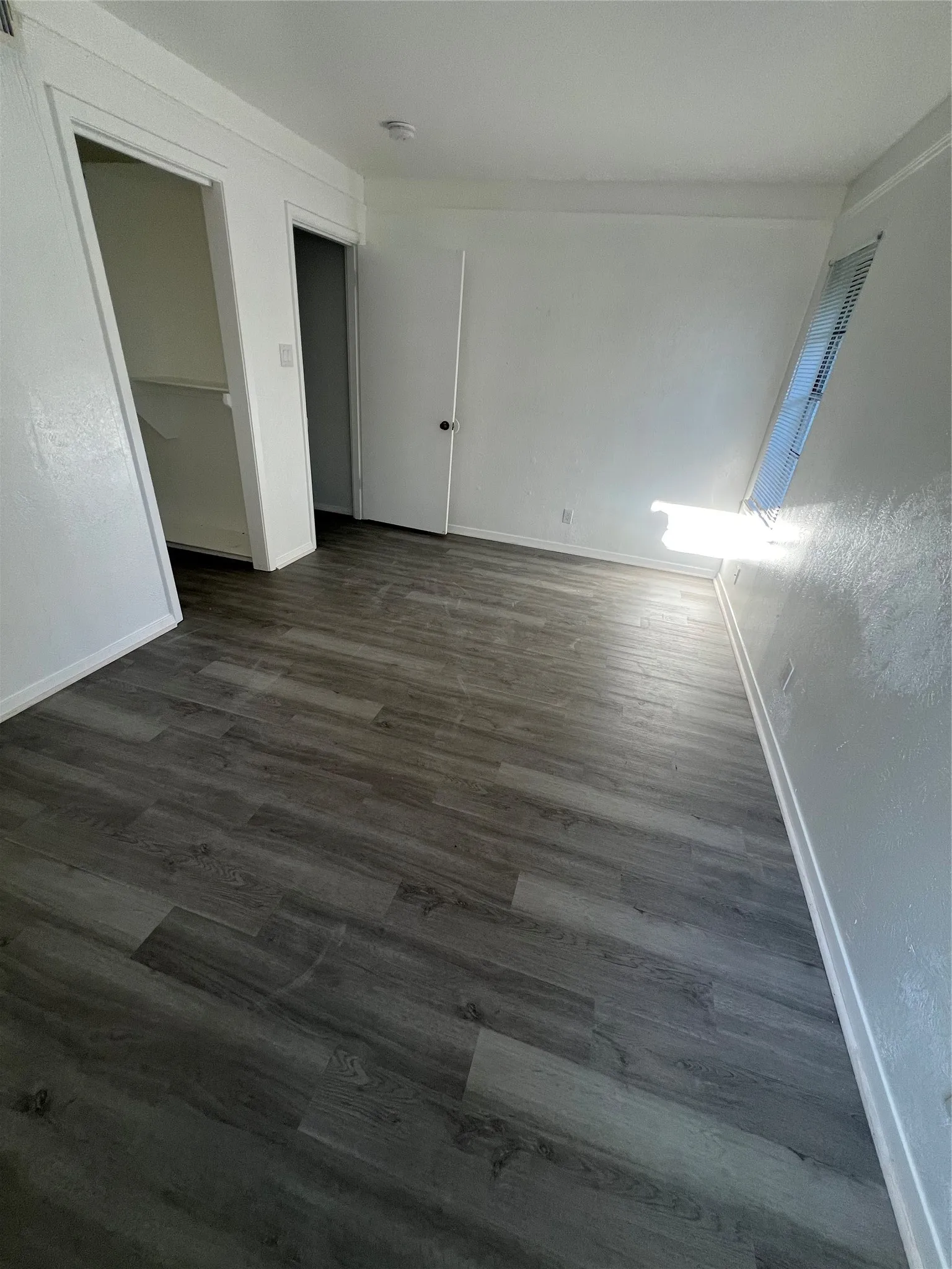 Neutral-toned wood-finish flooring, white walls, and a window with horizontal blinds
