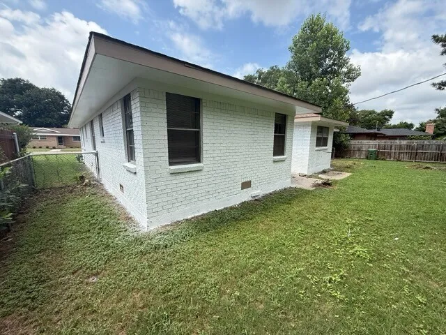 Exterior featuring painted white brick siding, a mono-pitch roofline, and an expansive side yard with perimeter wood fencing
