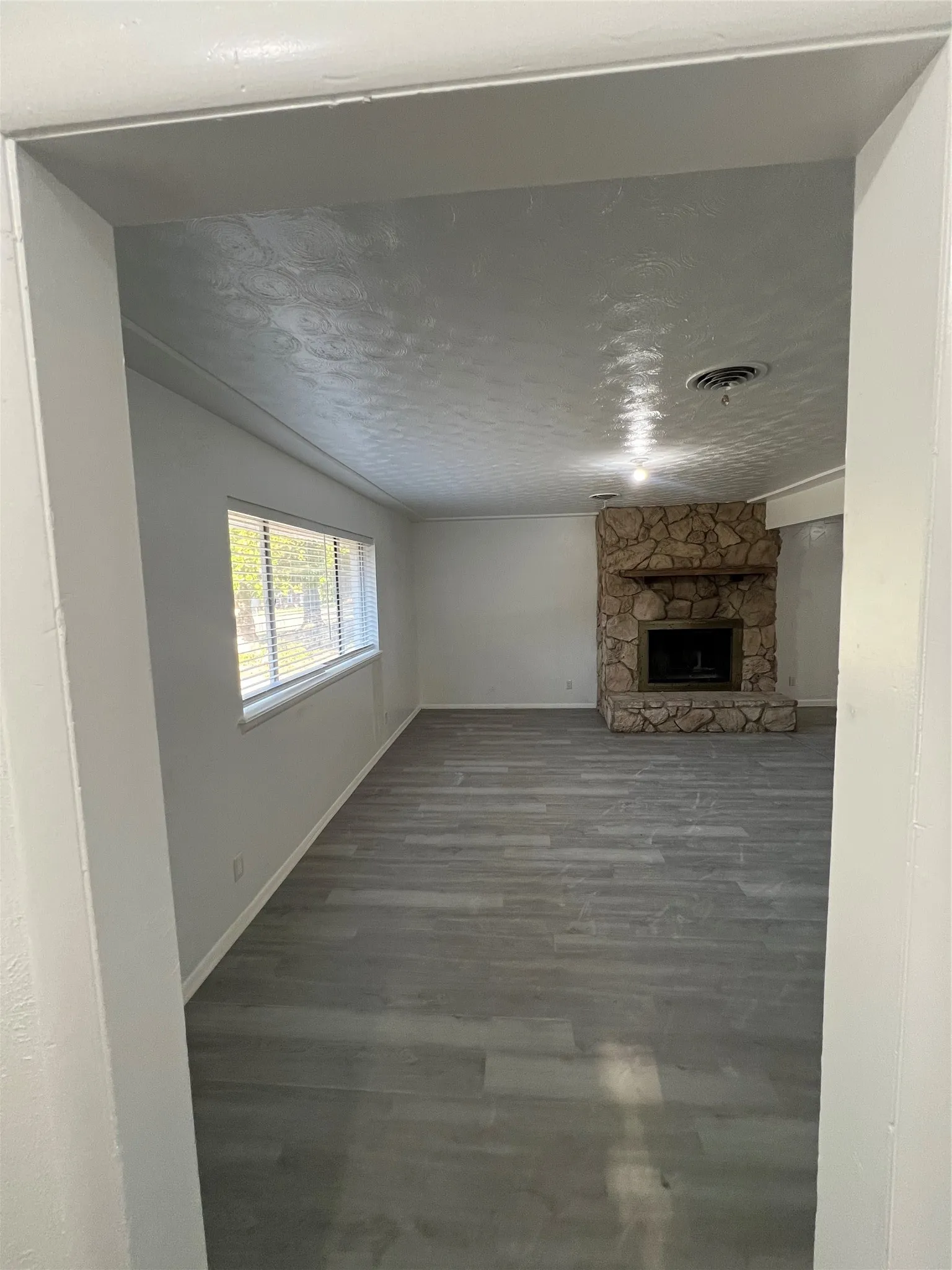 Interior space featuring wood-finish flooring, a floor-to-ceiling stone fireplace, a timber mantel, and horizontal window blinds