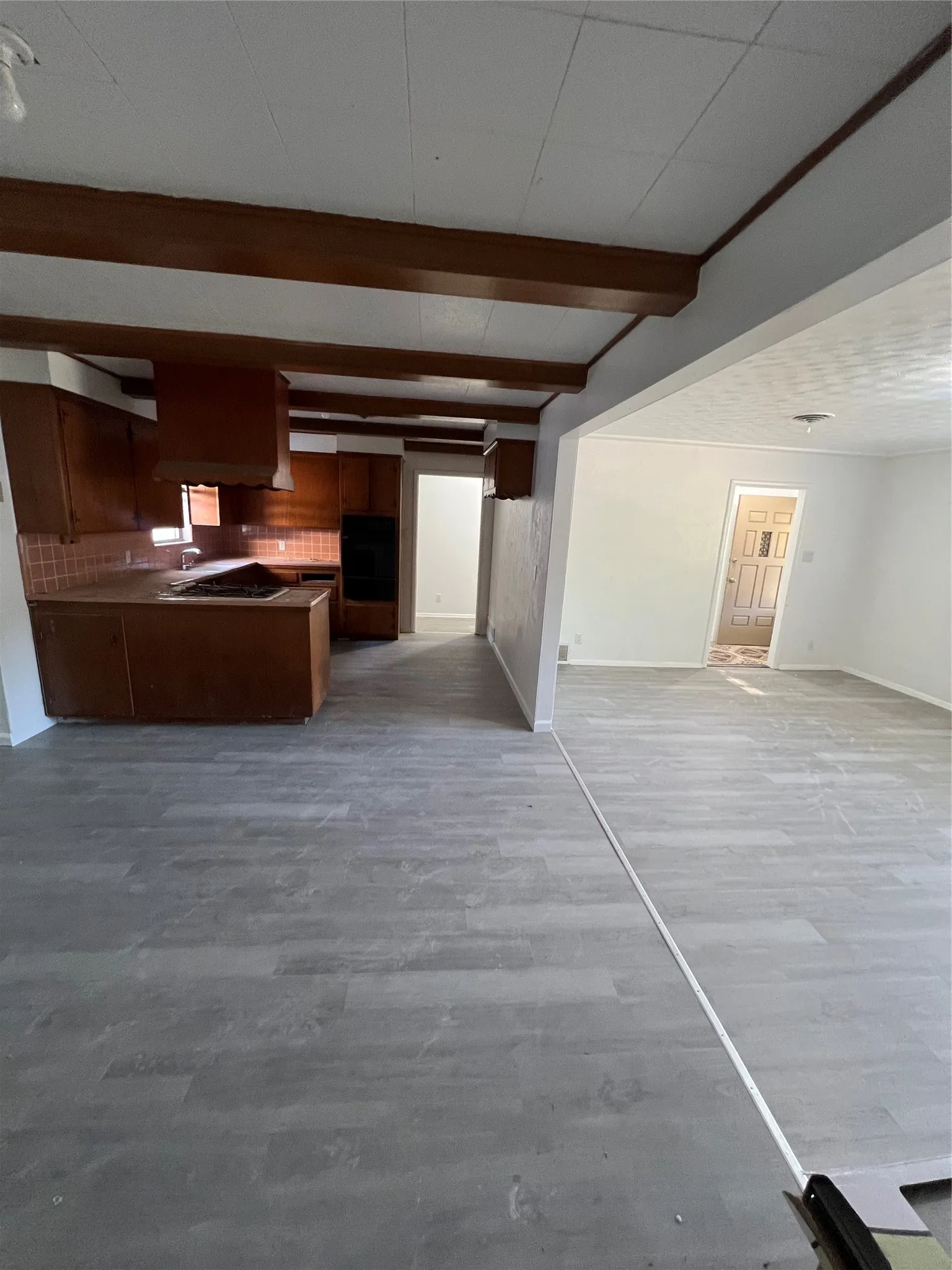 Interior featuring wood-finish flooring, exposed ceiling beams, built-in cabinetry, tile backsplash, and a wall-mounted oven