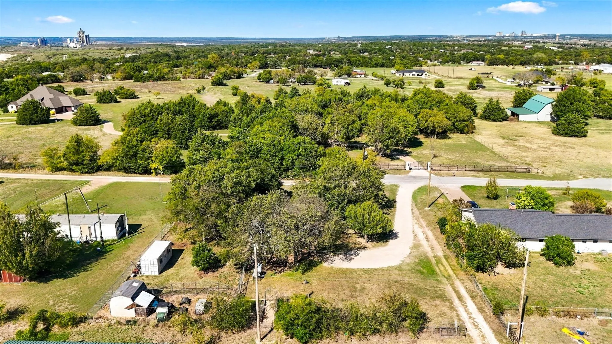Expansive parcel featuring mature trees, a gravel driveway, perimeter fencing, and open acreage