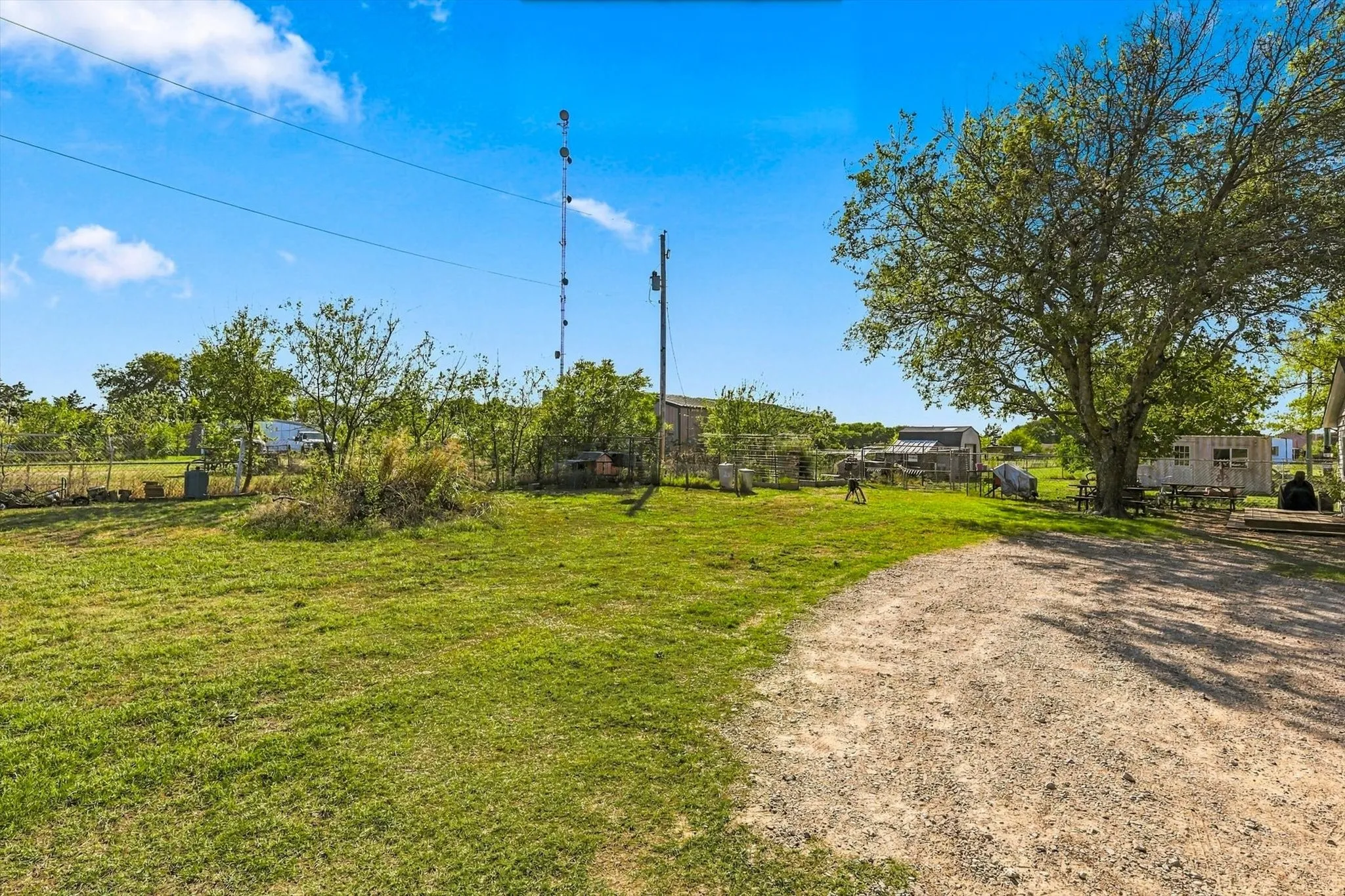 Expansive grounds featuring a gravel driveway, open green space, mature trees, and perimeter fencing