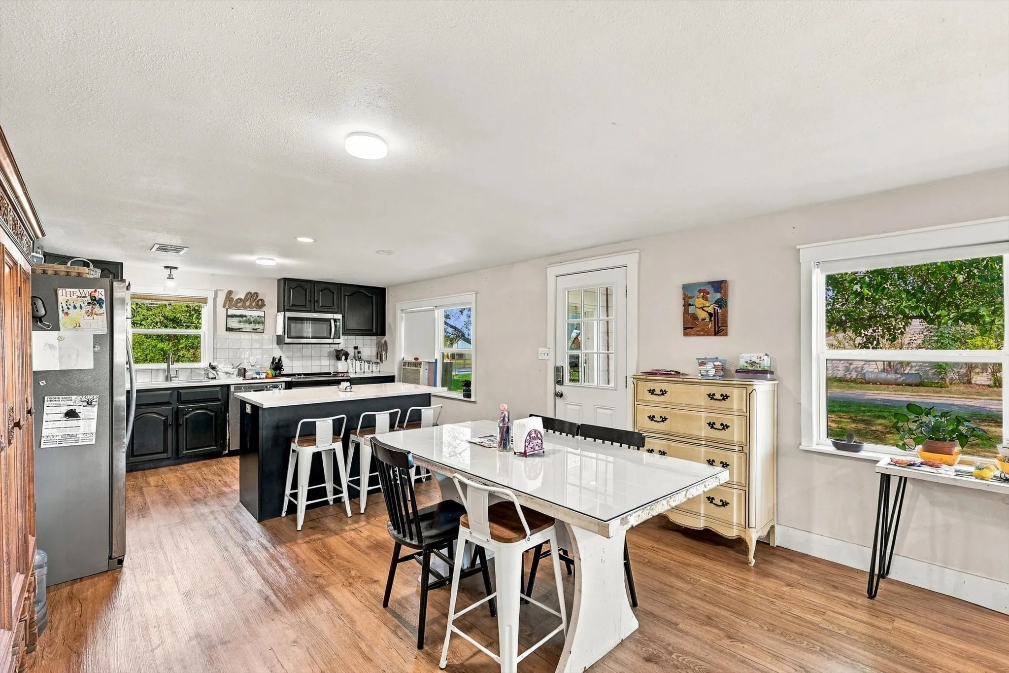 Kitchen featuring black cabinetry, a white central island with counter seating, stainless steel appliances, wood-finish flooring, and multiple windows