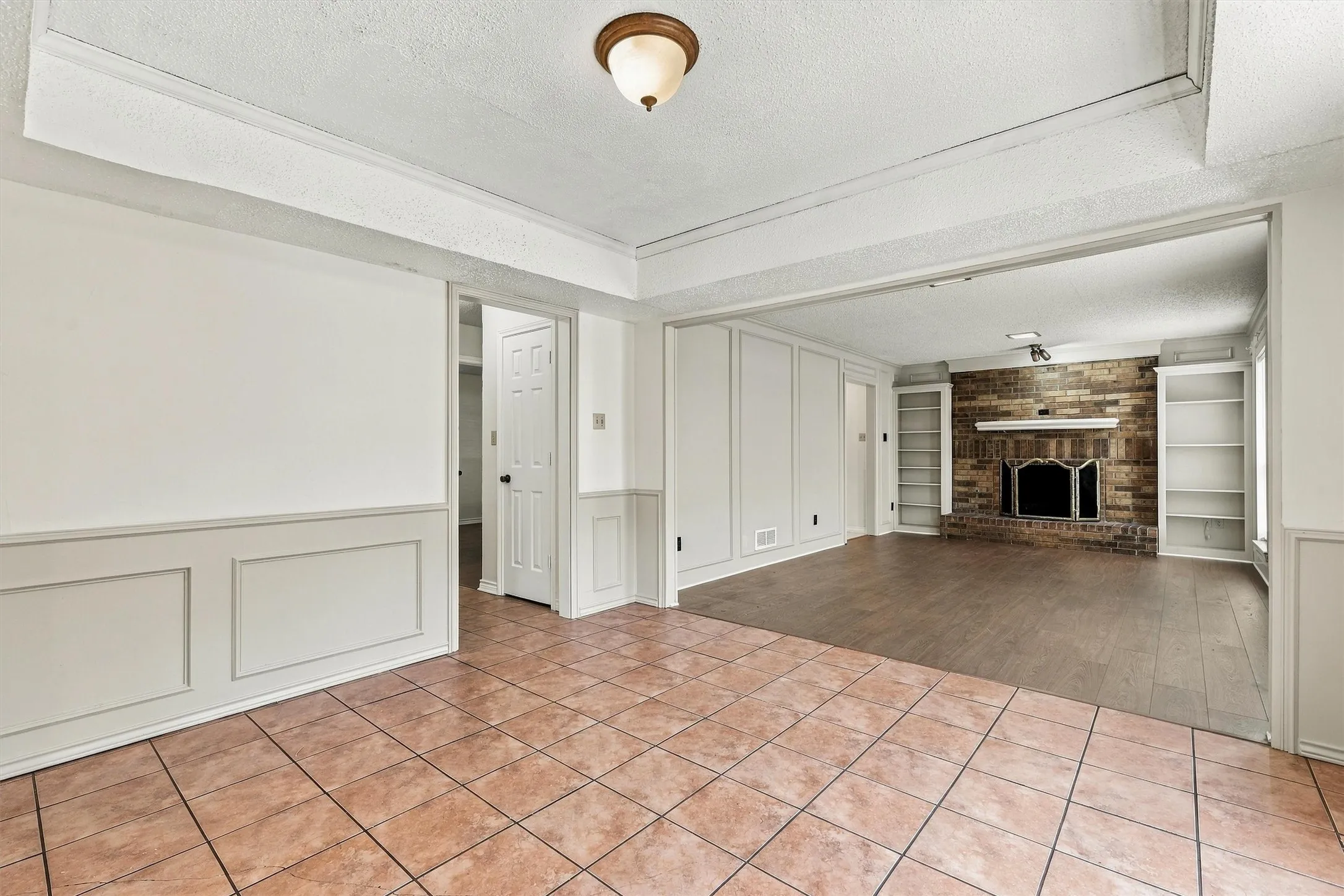 Interior featuring tray ceilings, wainscoting, tile flooring, wood-finish flooring, and a brick fireplace with built-in shelving