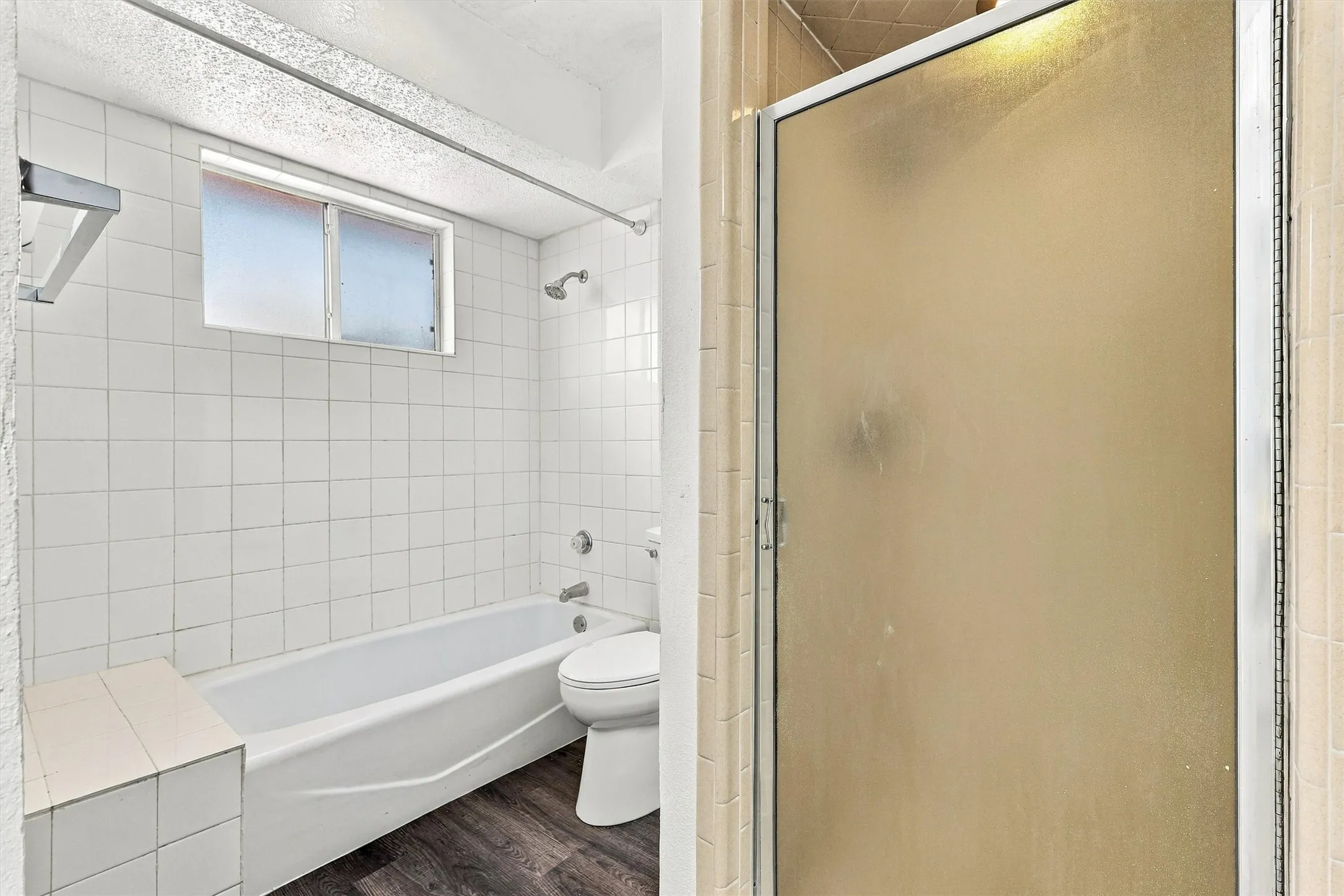 Bathroom featuring a built-in bathtub with a tile surround, separate shower enclosure with a glass door, wood-finish flooring, and a window