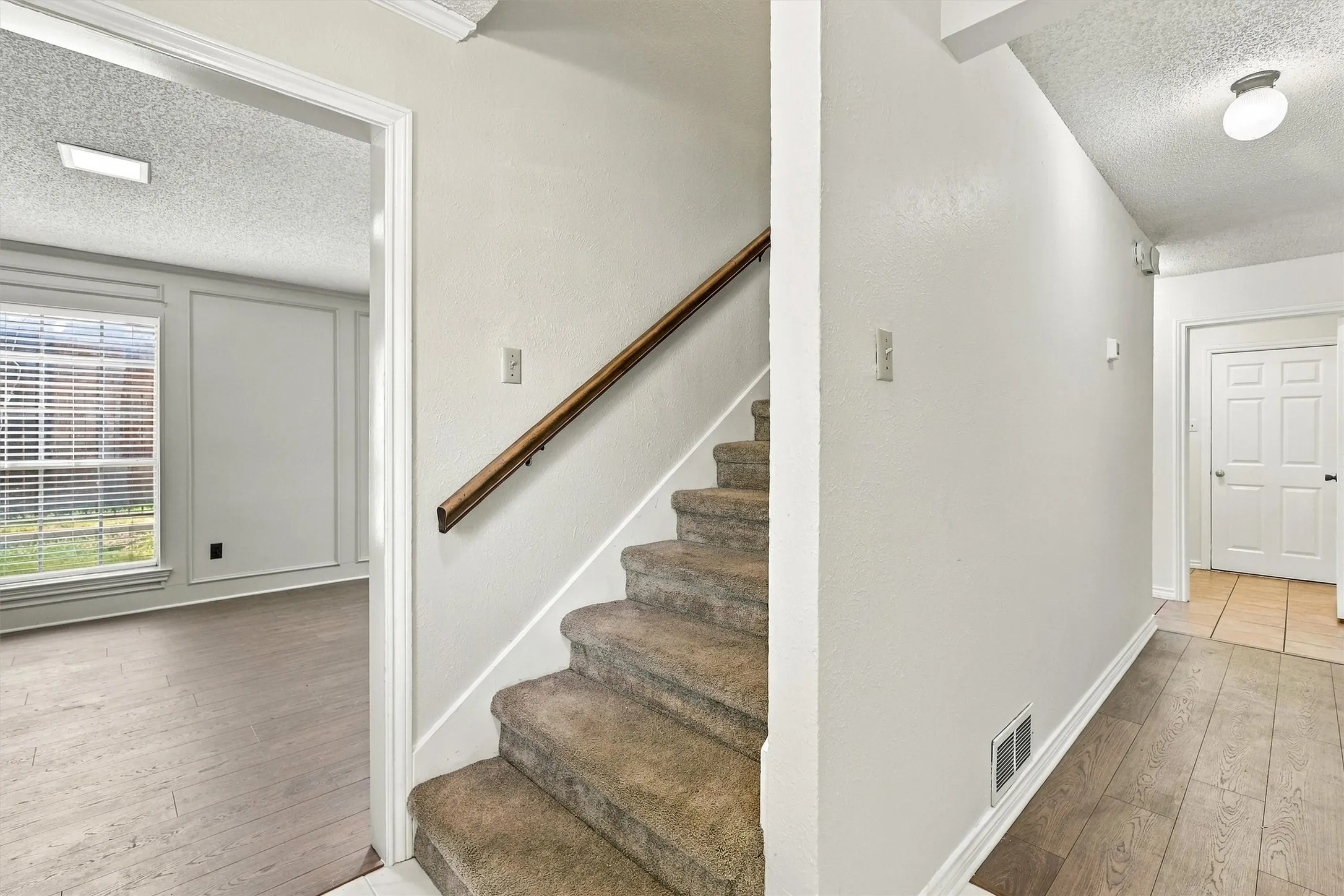 Carpeted staircase with a wood handrail, wood-finish flooring, paneled wall detailing, and a multi-panel door