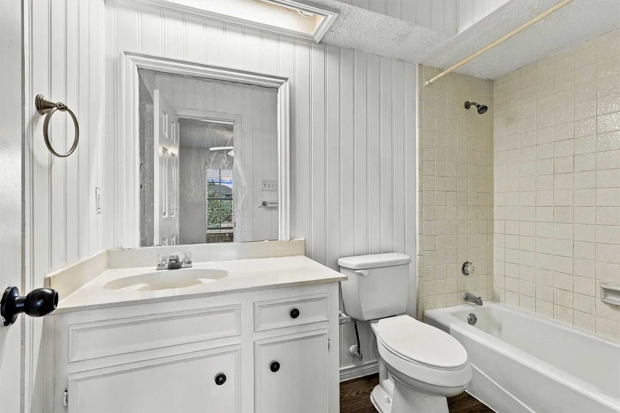 Bathroom featuring vertical plank wall paneling, a white vanity with an integrated sink, a framed mirror, a skylight, and a tiled shower surround