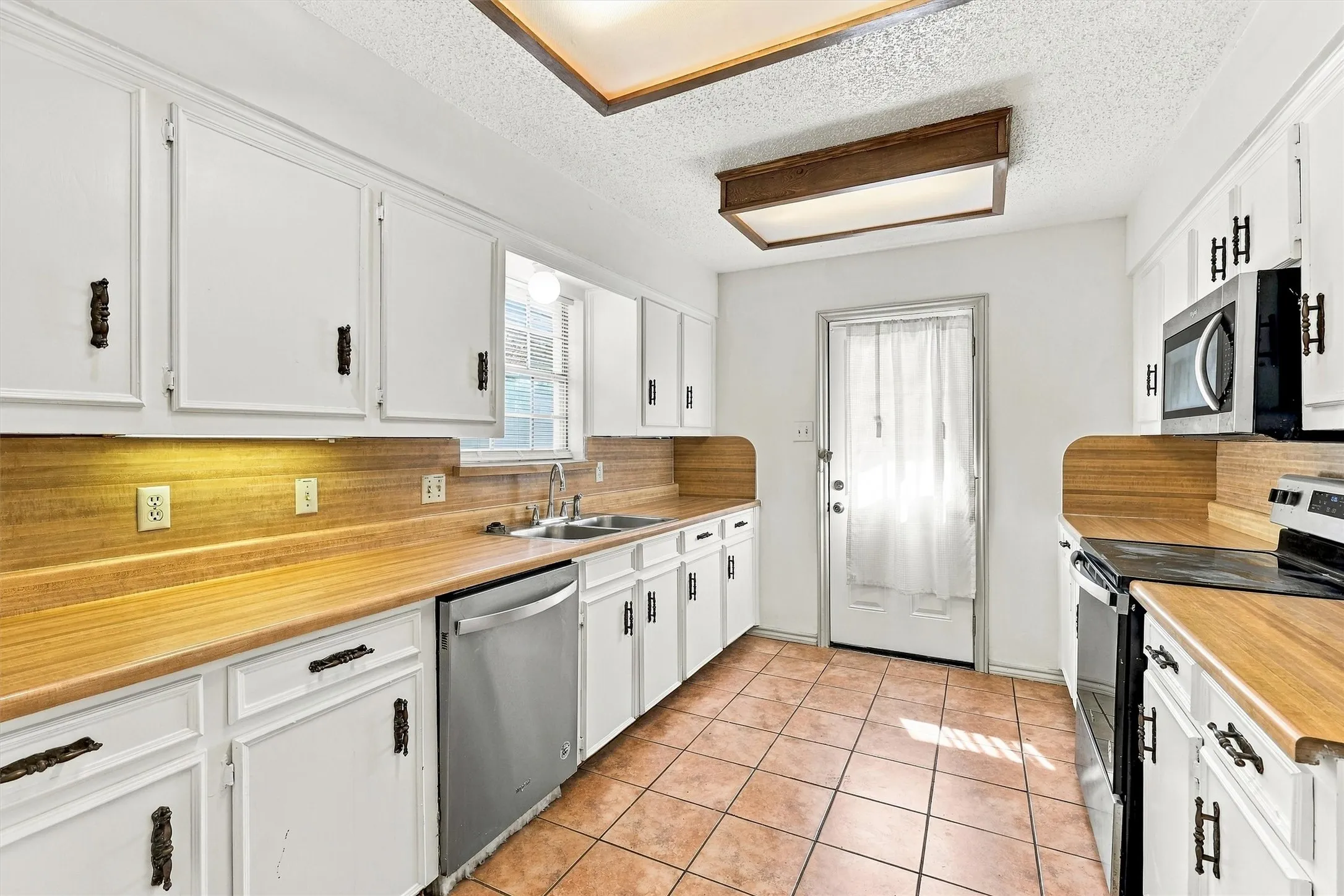 Kitchen featuring white shaker-style cabinetry, wood-finish countertops with matching backsplashes, ceramic tile flooring, and stainless steel appliances
