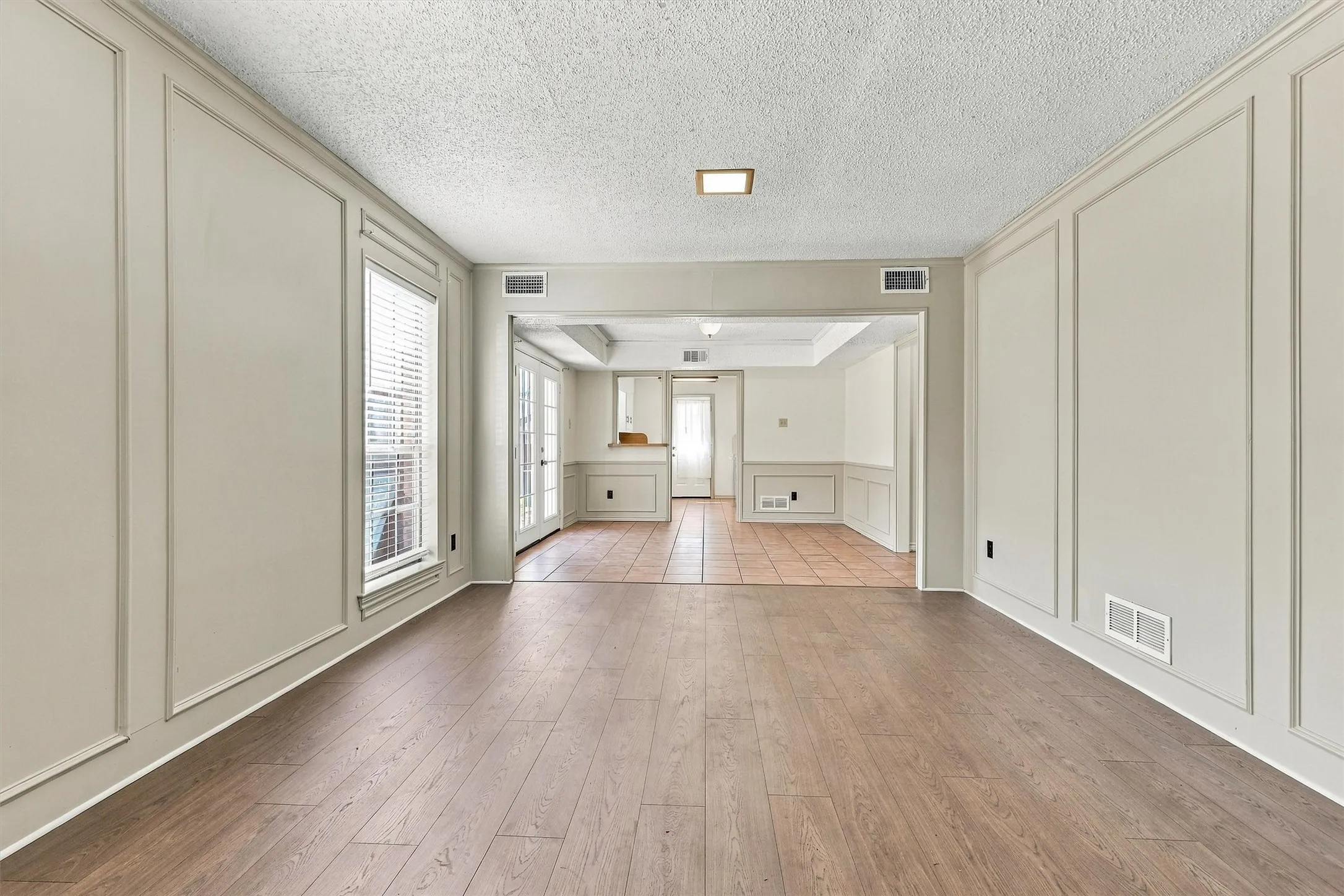 Room featuring wood-finish flooring, decorative wall molding, and tiled surfaces with French doors