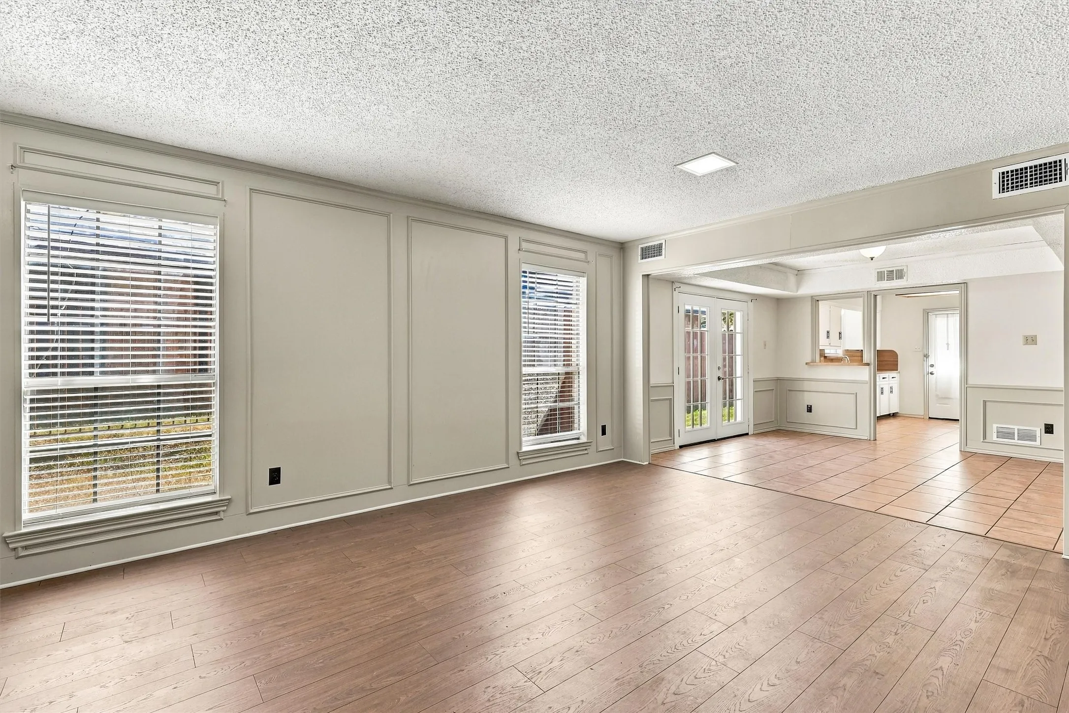 Living area featuring wood-finish flooring, wainscoting, decorative wall molding, large dual-pane windows, and tile flooring