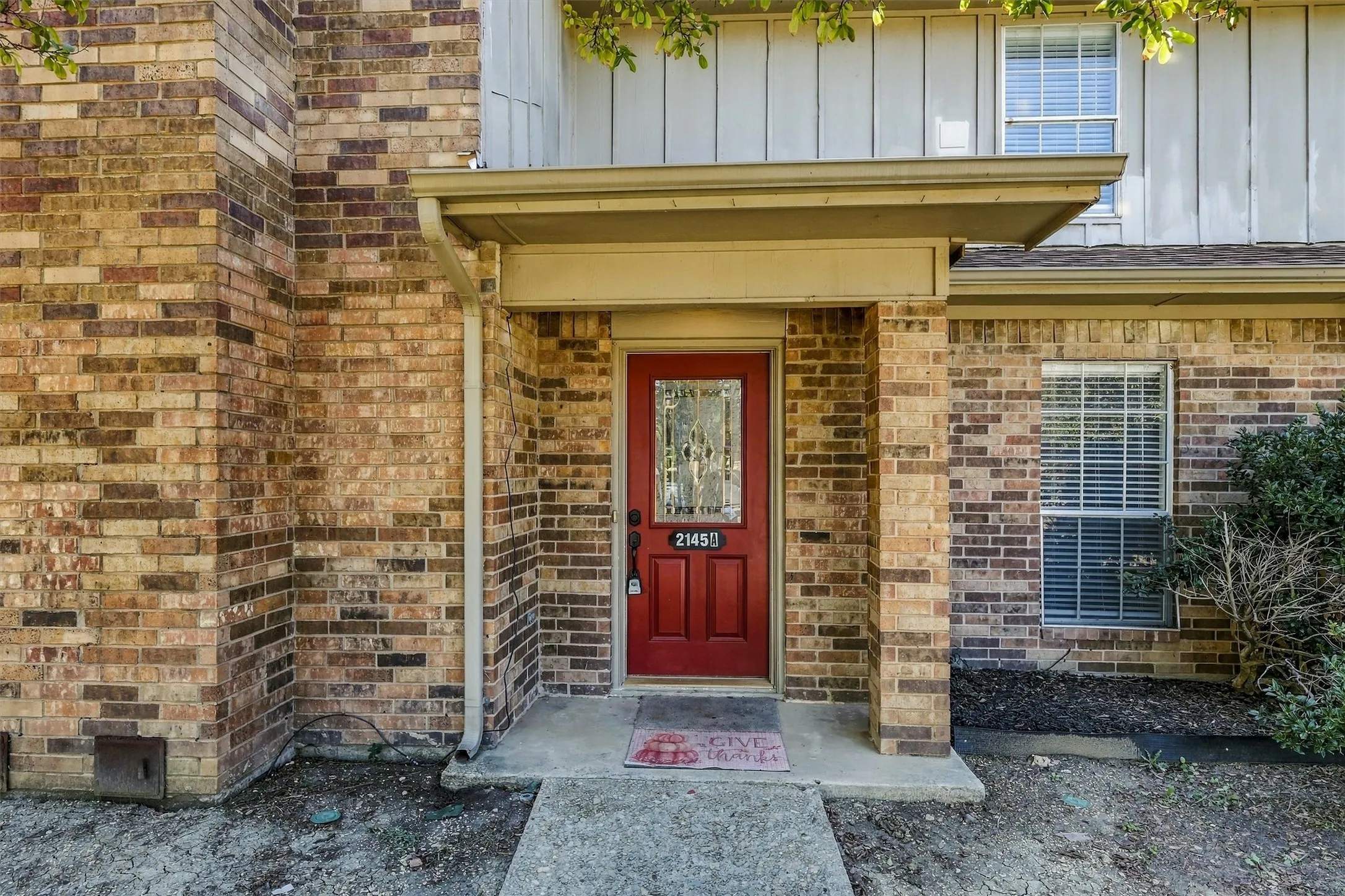 Exterior facade featuring multi-tonal brick masonry, vertical siding, a covered entryway, and a red front door with a decorative glass insert