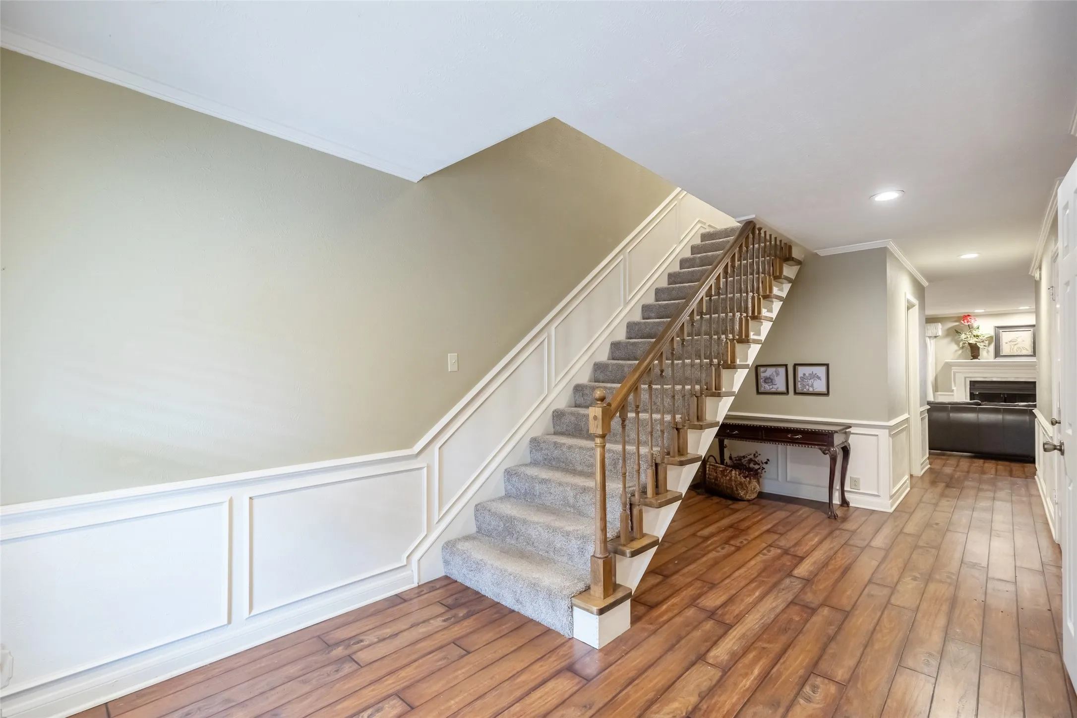 Staircase featuring wood railings and carpeted treads, complemented by decorative wall molding, wood-finish flooring, and recessed ceiling lighting