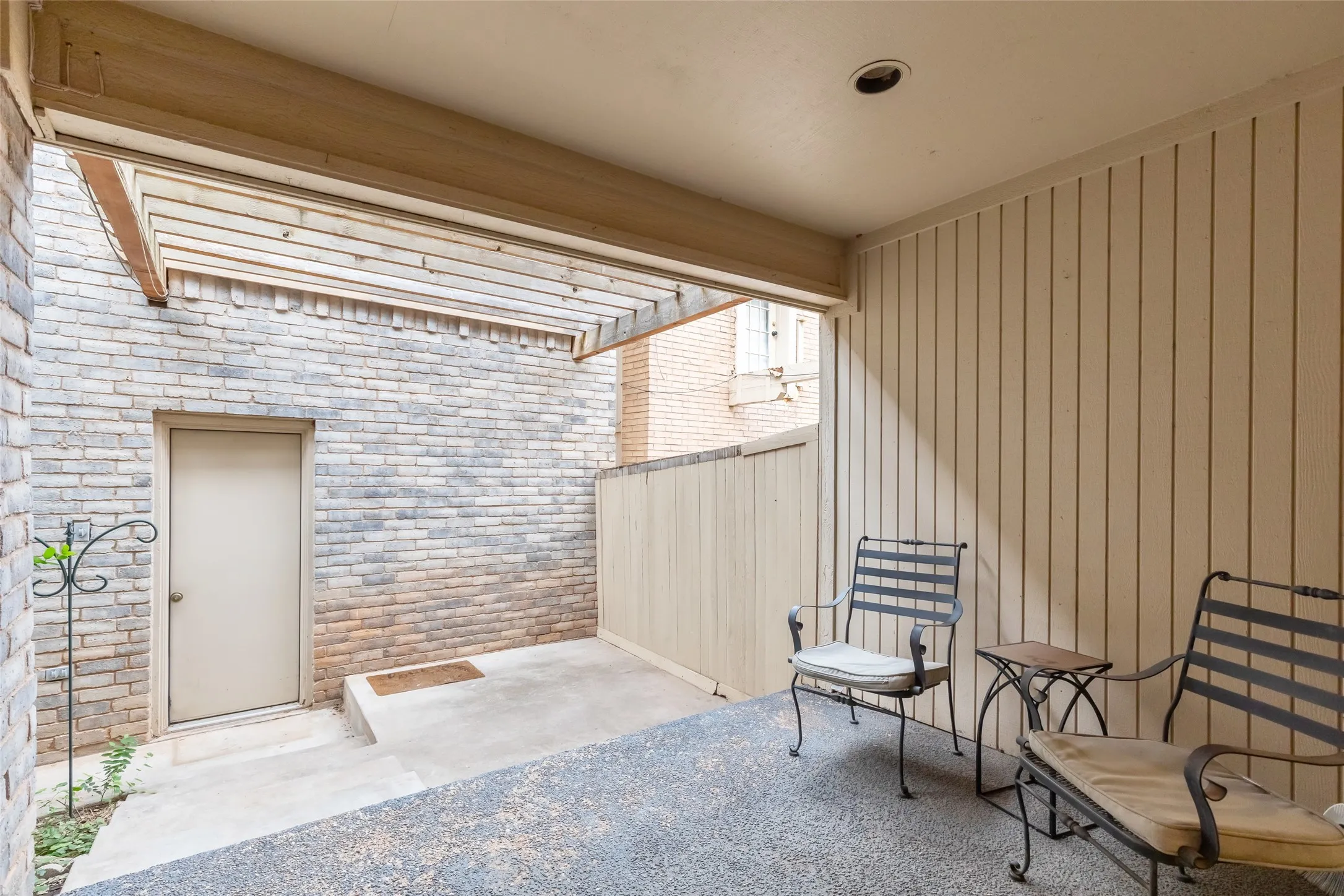 Covered patio featuring an exposed-beam pergola, concrete flooring, vertical wood-panel siding, and brick masonry exterior walls