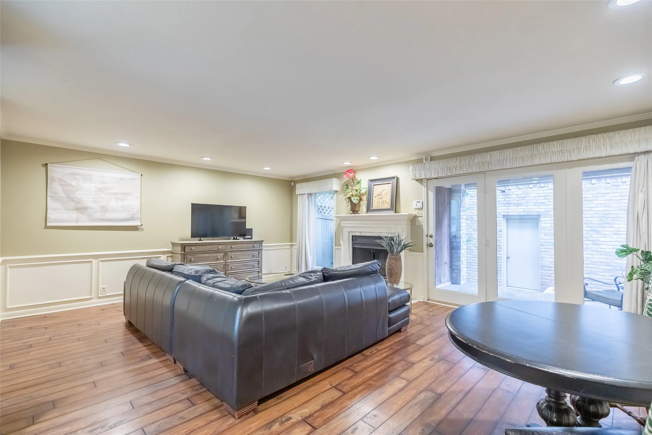 Living area featuring wood-finish flooring, wainscoting, recessed lighting, and a fireplace with a decorative mantel, including multi-pane glass doors