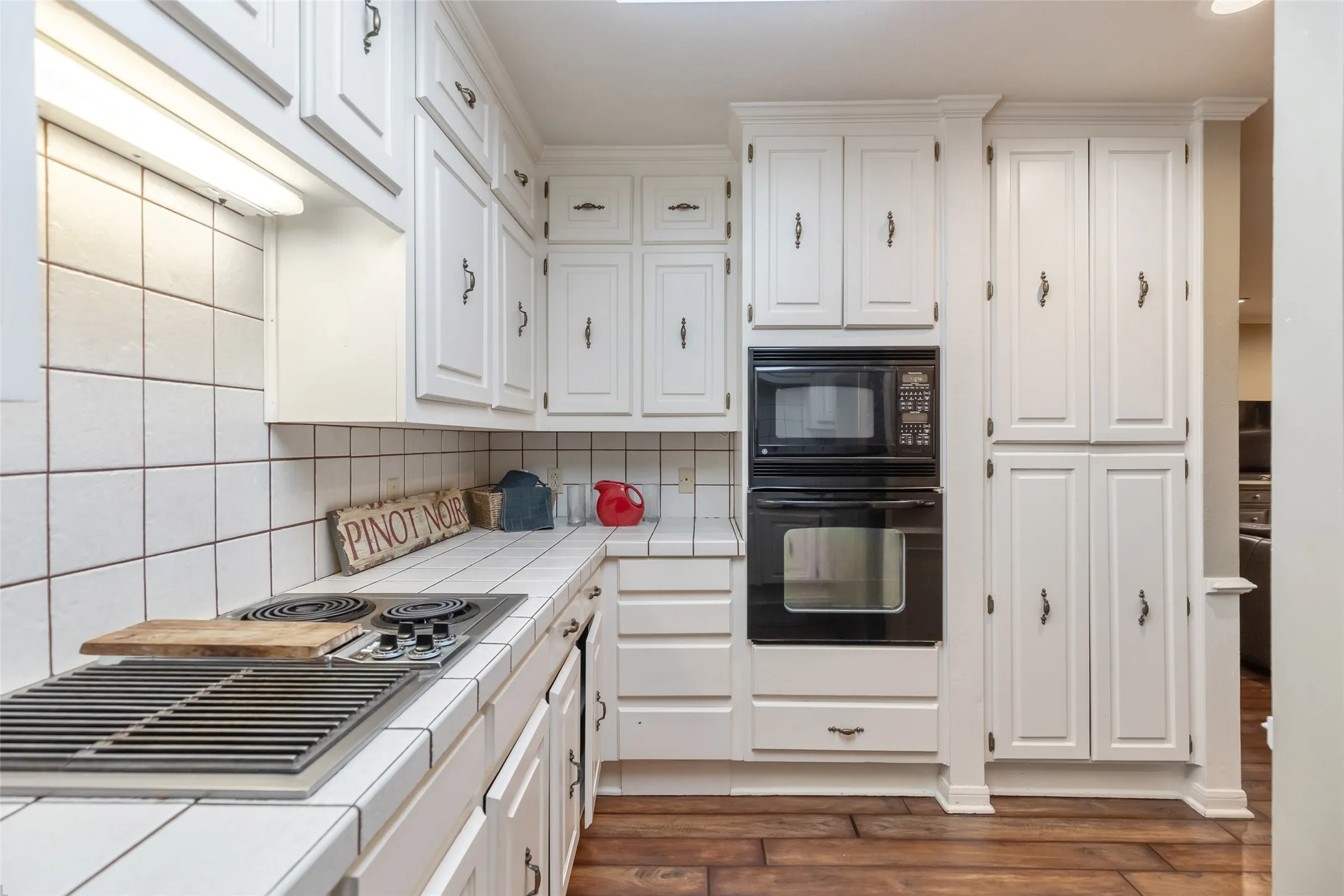 Kitchen featuring white cabinetry, wood-finish flooring, square tile countertops and backsplash, and integrated double wall ovens