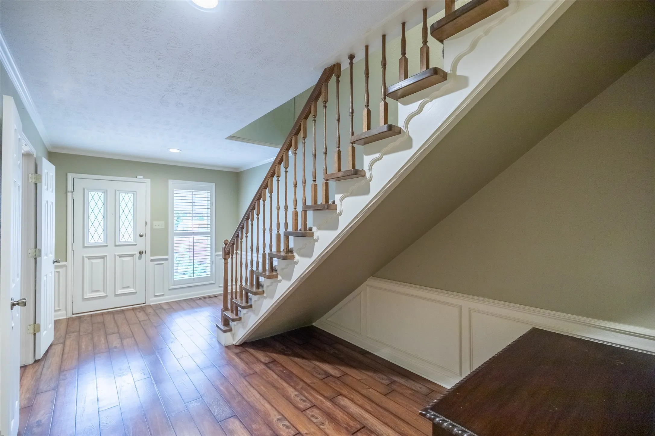 Staircase featuring wood-finish treads and a decorative balustrade, wood-finish flooring, wainscoting, and an exterior door with dual glass inserts