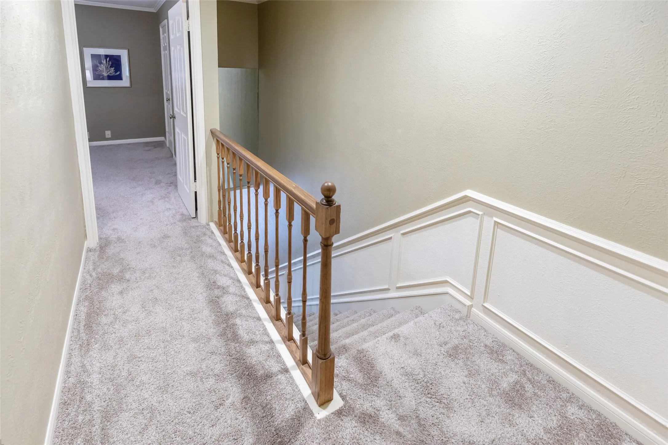 Staircase featuring wood railings and balusters with white wainscoting paneling and neutral carpeting