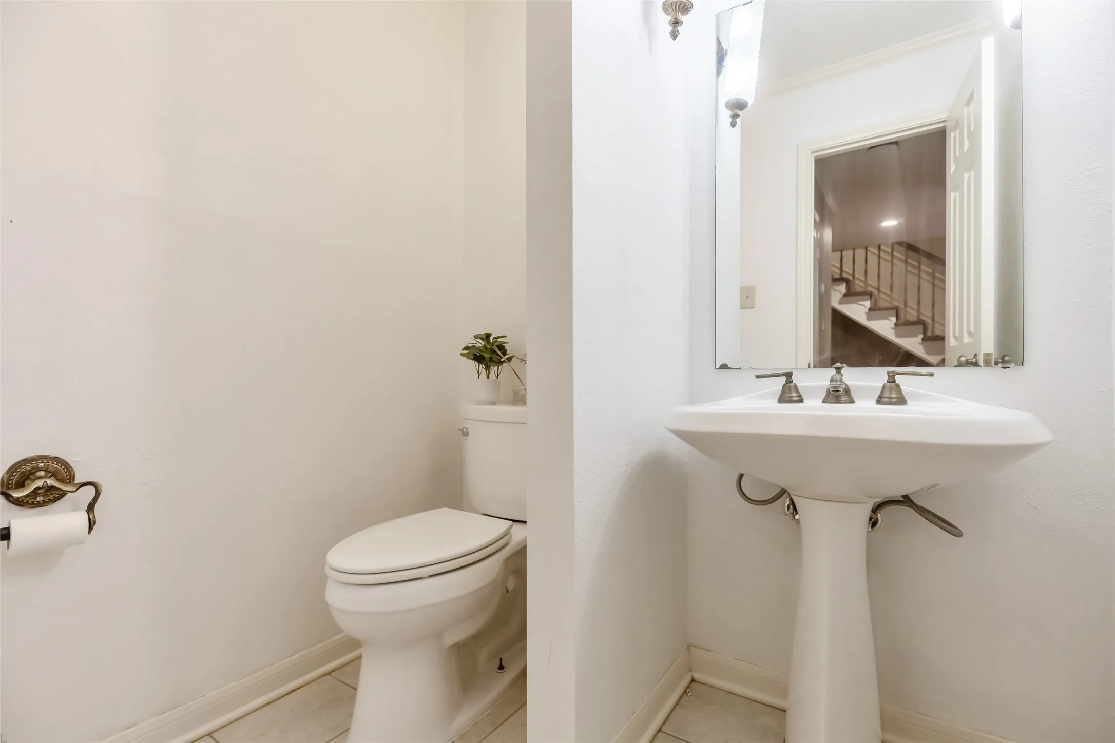 Pedestal sink with a widespread faucet, wall-mounted mirror, and tile flooring