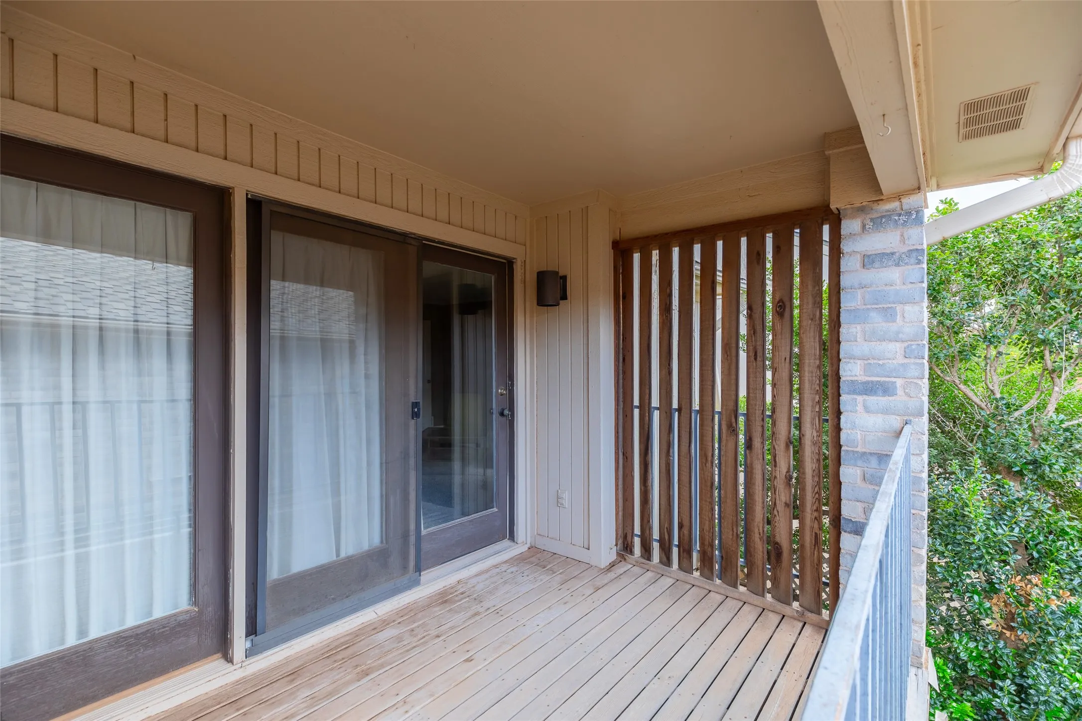 Covered balcony featuring wood-plank flooring, vertical wood slat privacy screening, a metal railing, and glass sliding door access