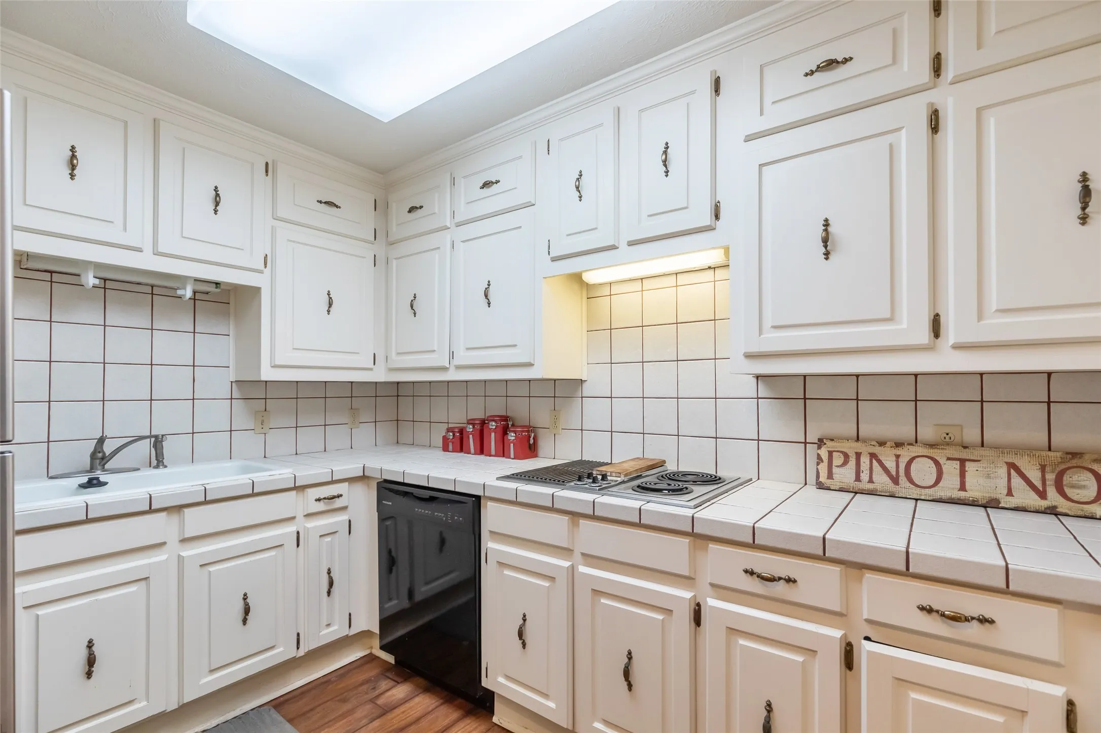 Kitchen featuring white cabinetry with brass-tone hardware, tile countertops, integrated backsplash, and wood-finish flooring