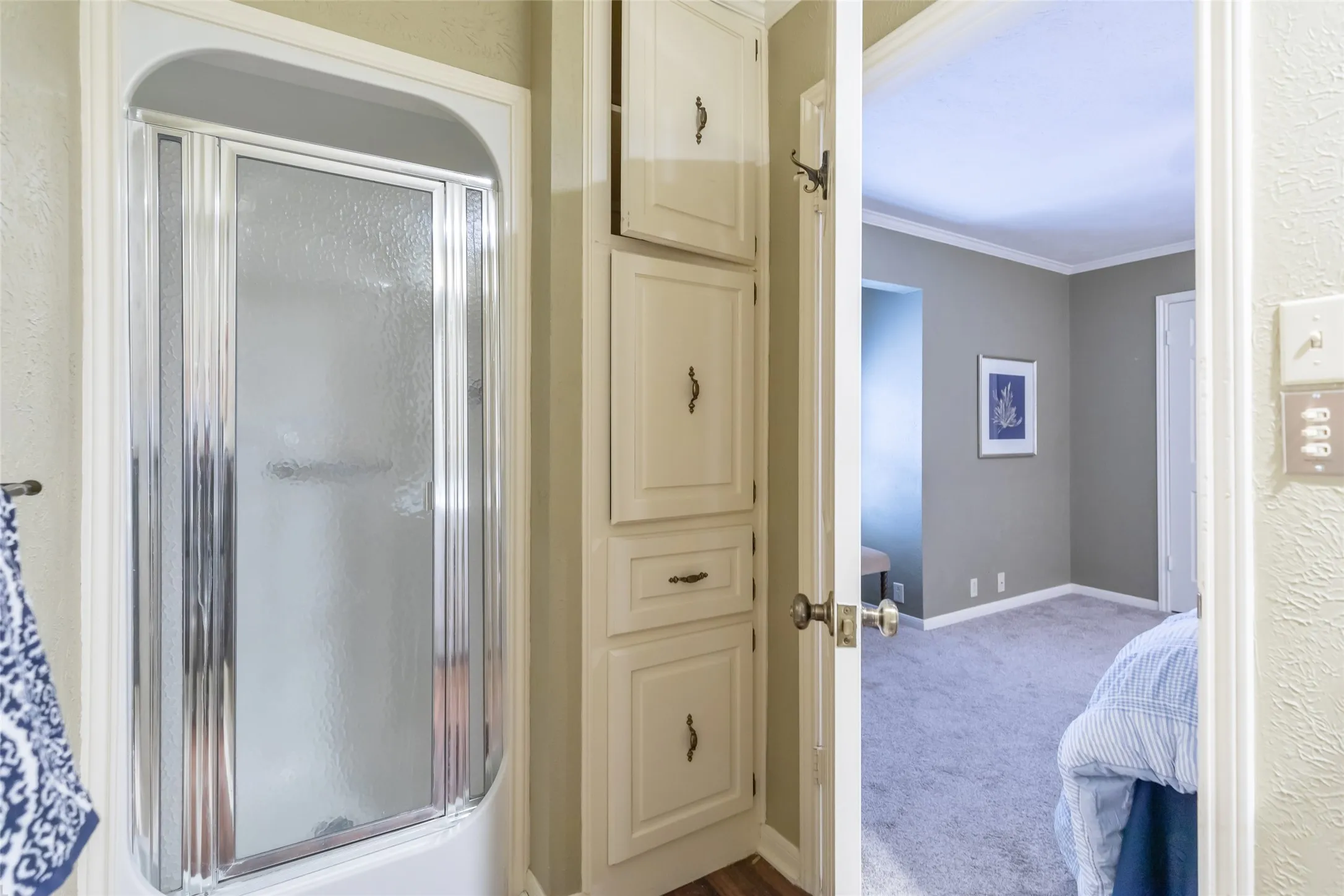 Shower stall featuring an arched chrome frame and textured glass enclosure, complemented by floor-to-ceiling built-in cabinetry with integrated drawers and oil-rubbed bronze hardware